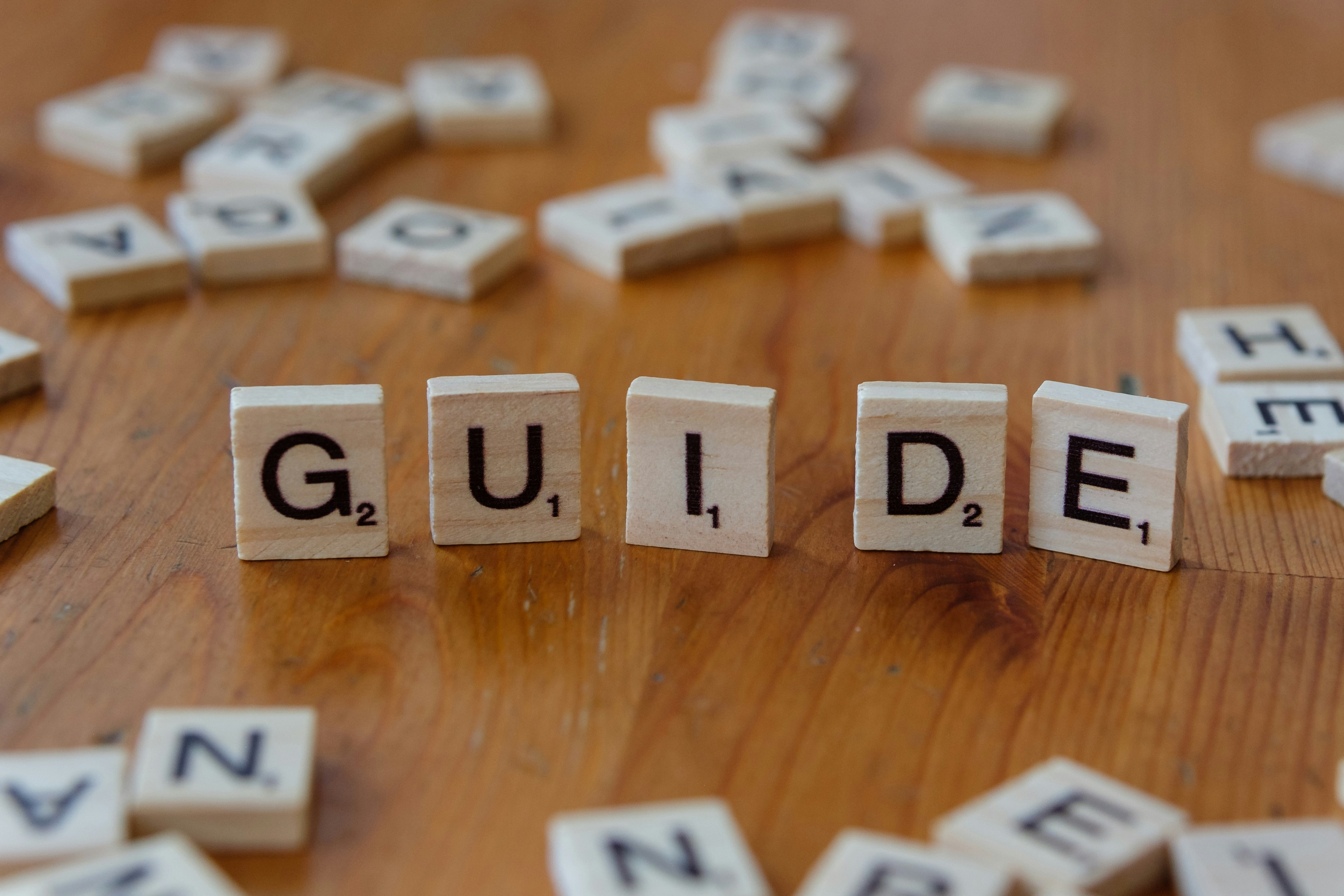 Photo presenting wooden letter tiles spelling “GUIDE” on a tabletop