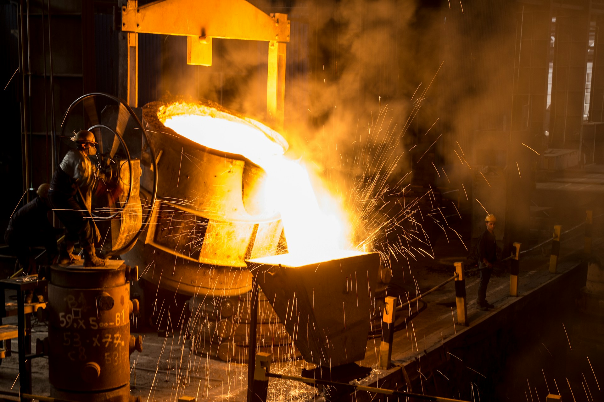 The photo presents workers pouring molten metal in a factory.