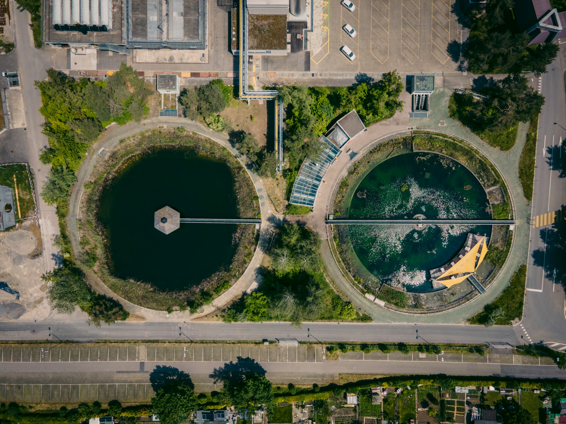 The photo presents an aerial view of a water treatment facility with circular settling ponds, pipelines, surrounding greenery and nearby roads.