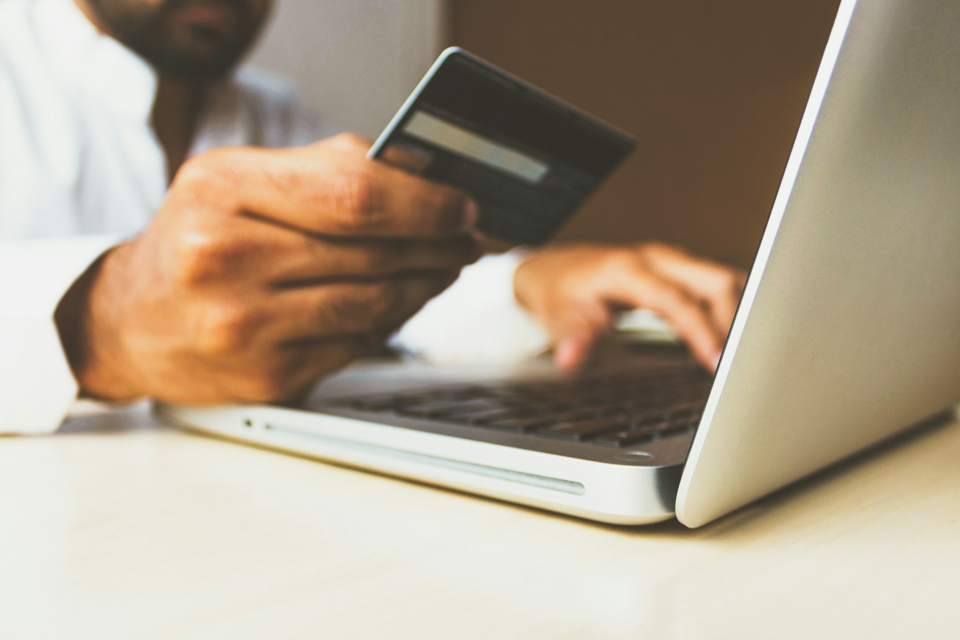 The photo presents a person holding a bank card while using a laptop.