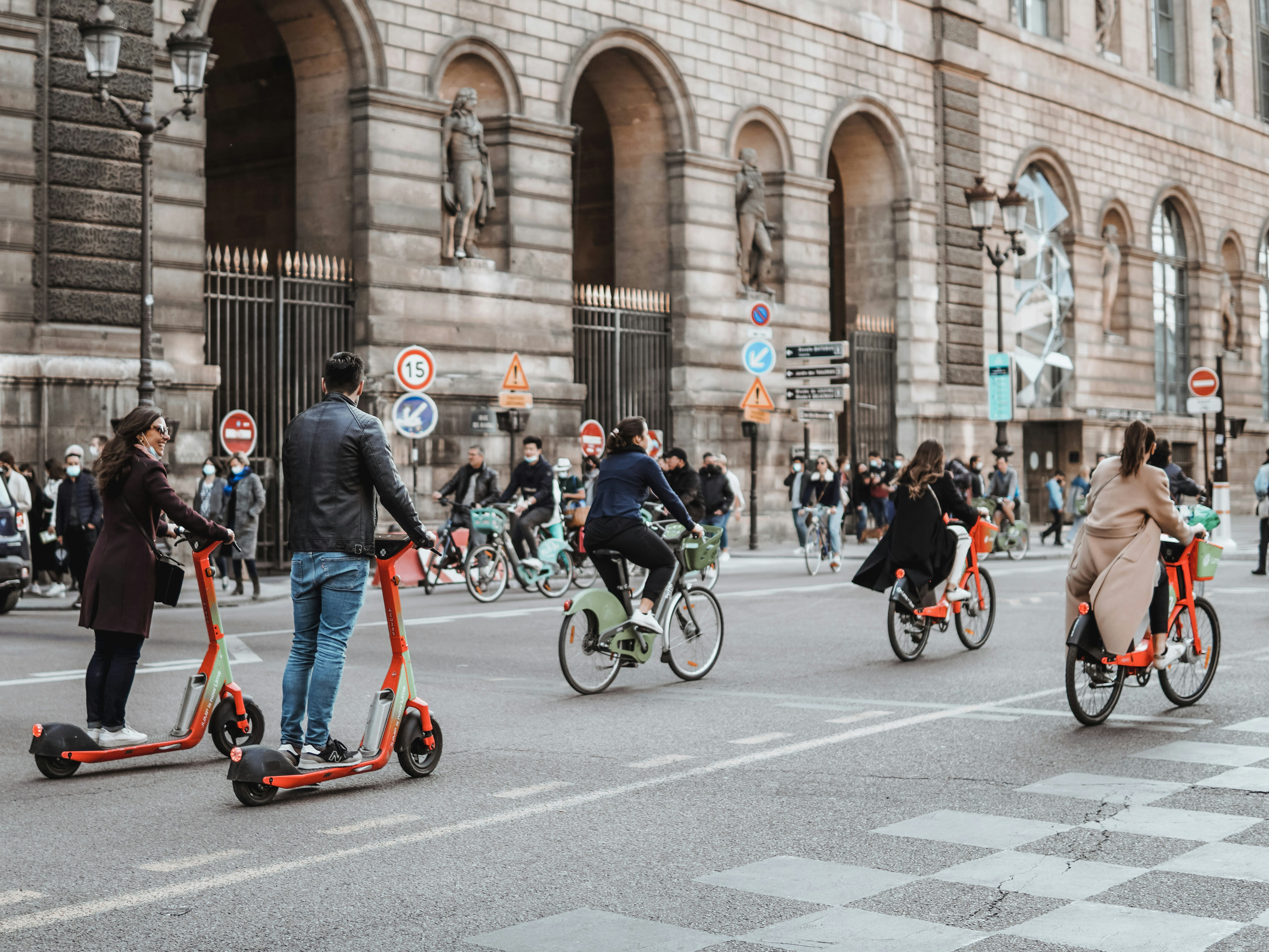 The picture shows people using bicycles and electric scooters in a busy urban street.