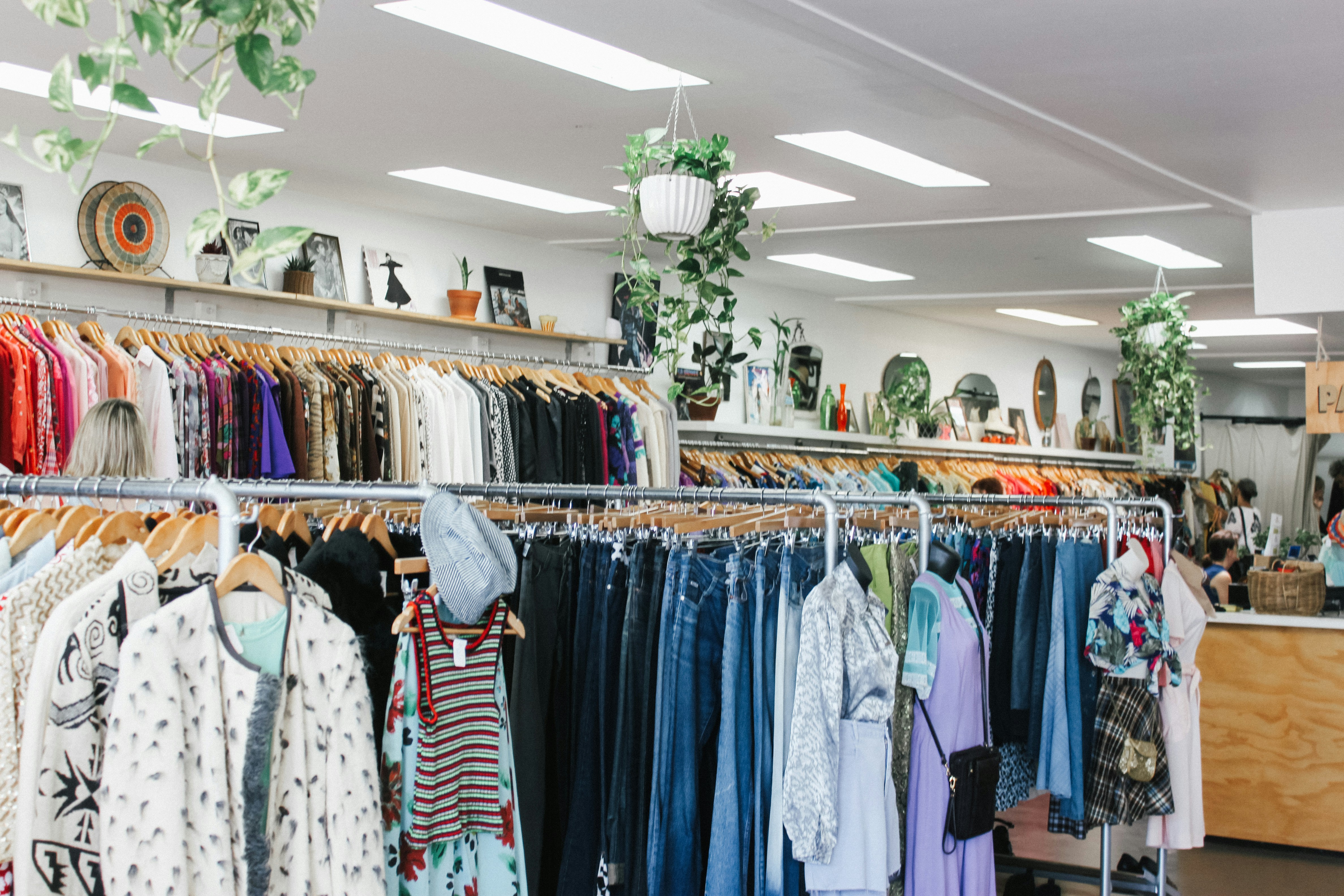 Colourful clothing hanging on racks inside a brightly lit clothing store. 