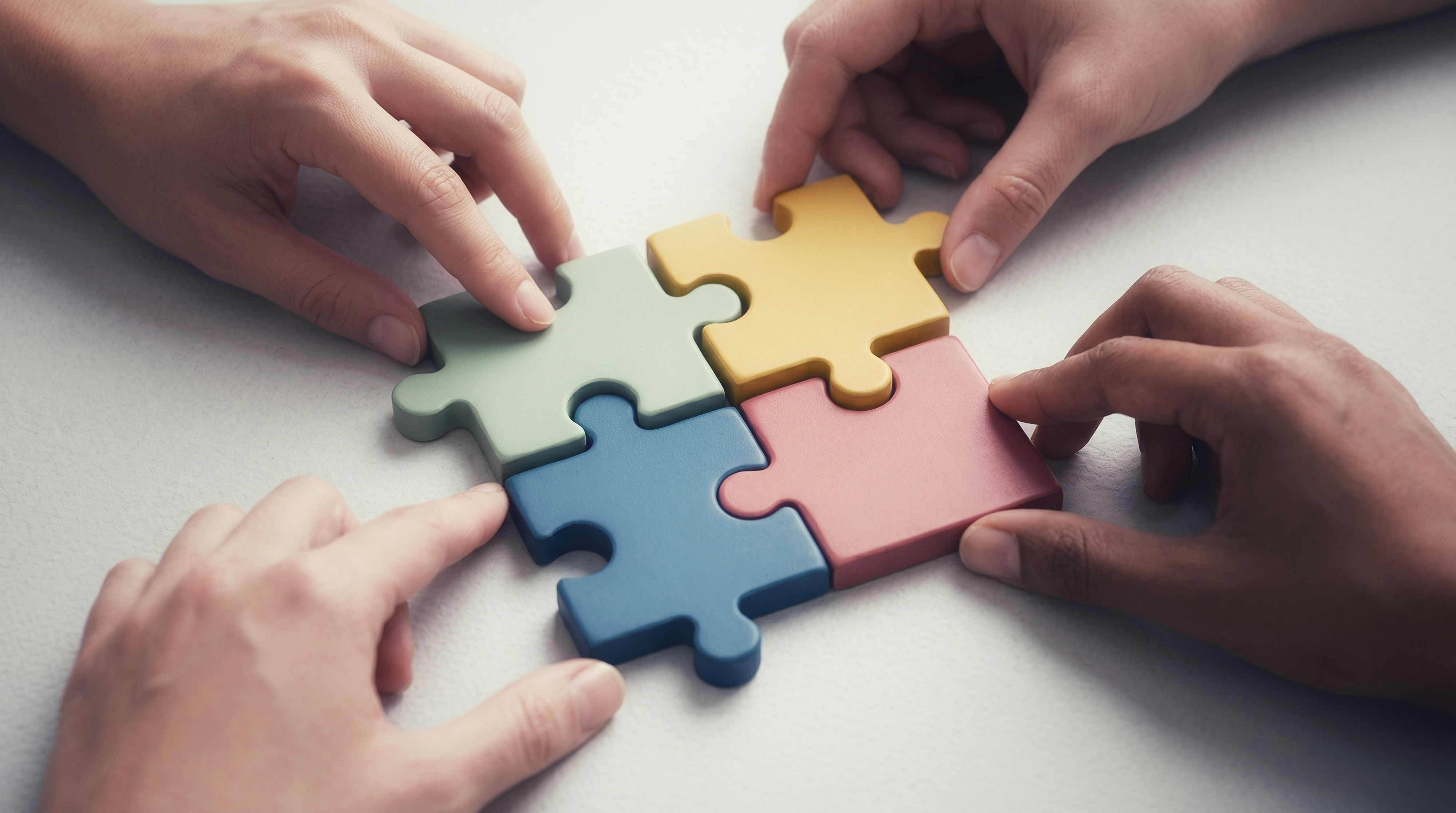 4 connected puzzle pieces in different colours and a hand holding each one