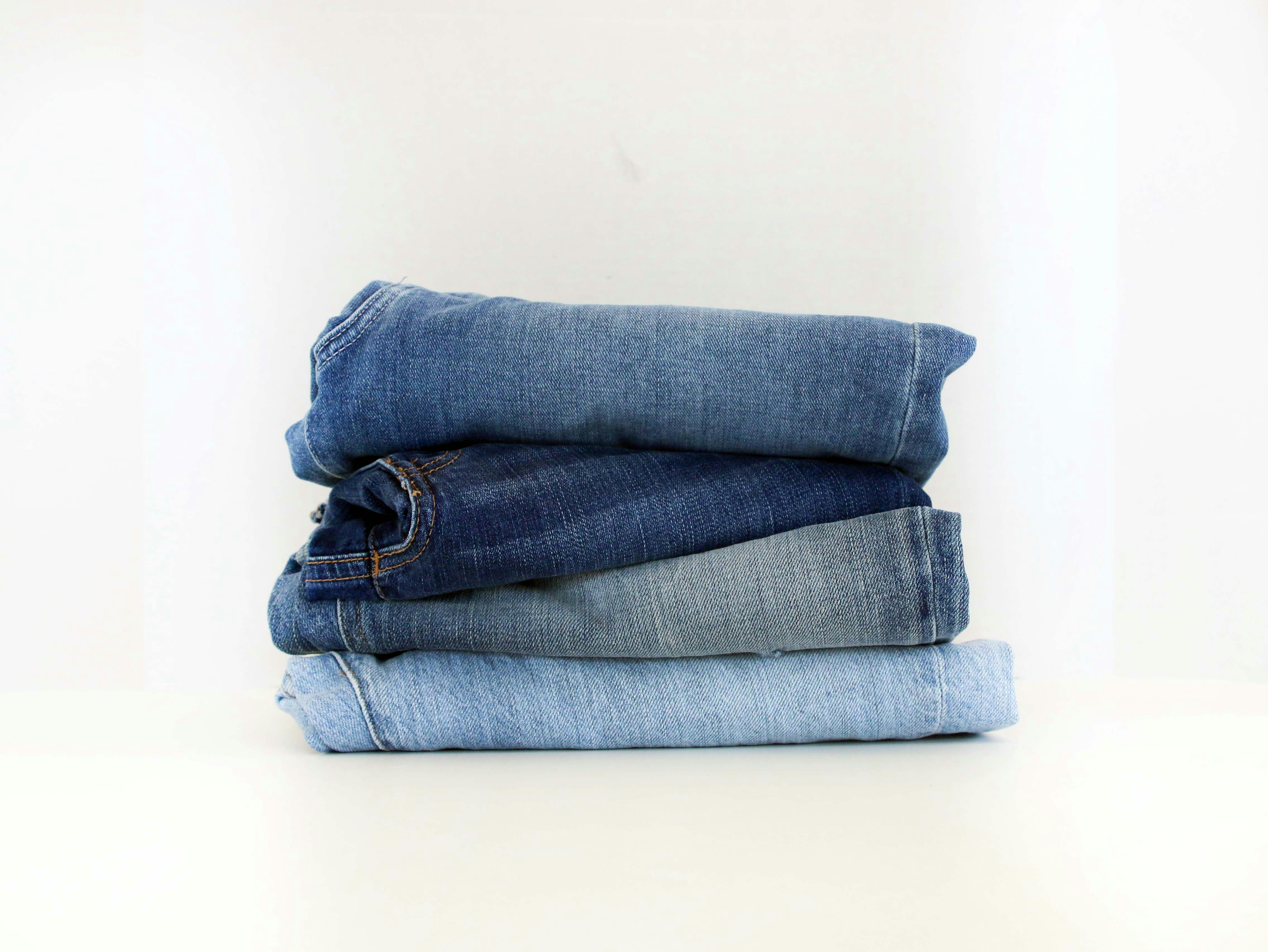 Stack of folded blue jeans in different denim washes, ranging from light to dark blue