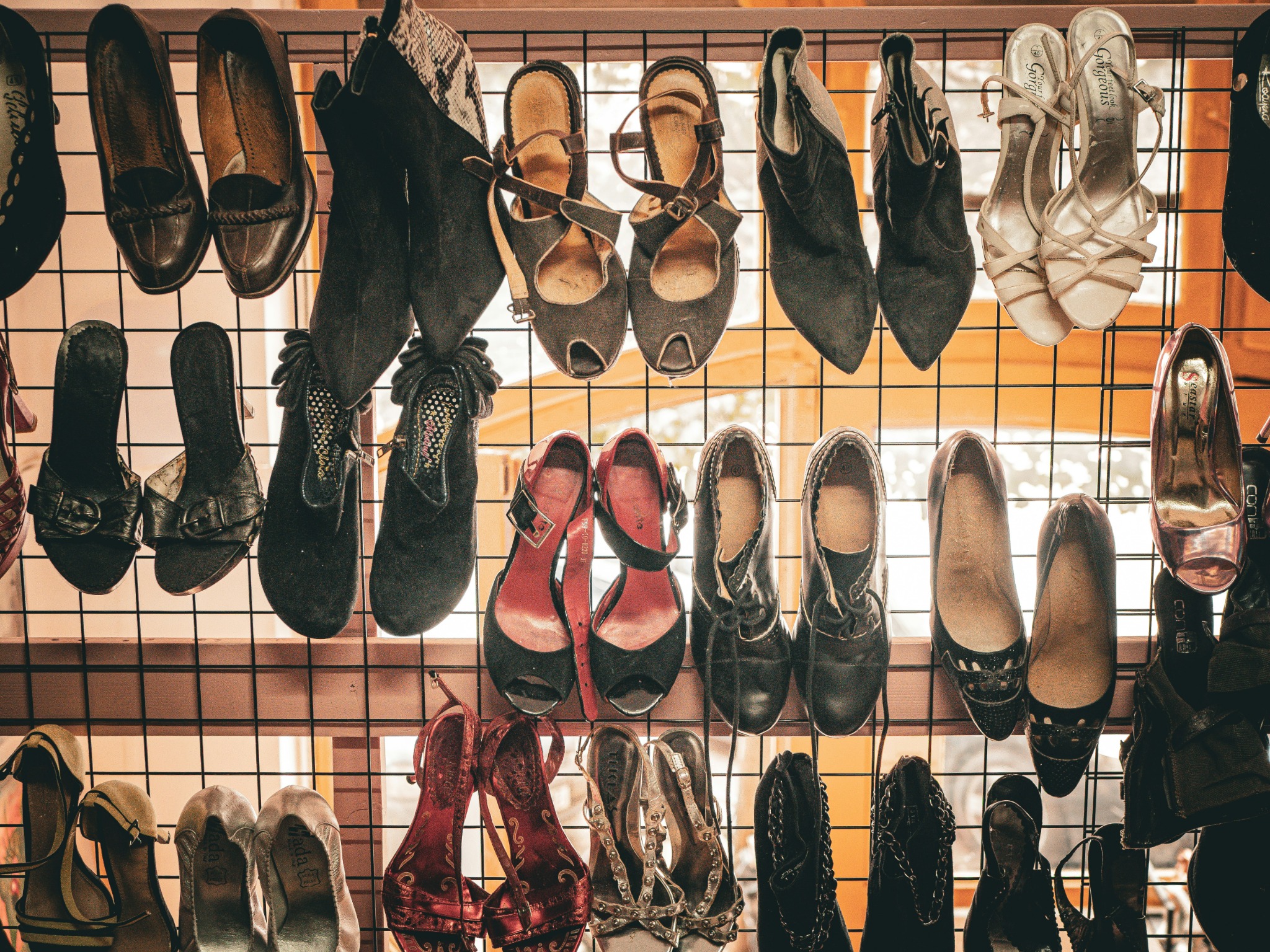 Various styles of women's footwear, including boots, sandals, heels and leather shoes, displayed on a metal rack in a retail setting.
