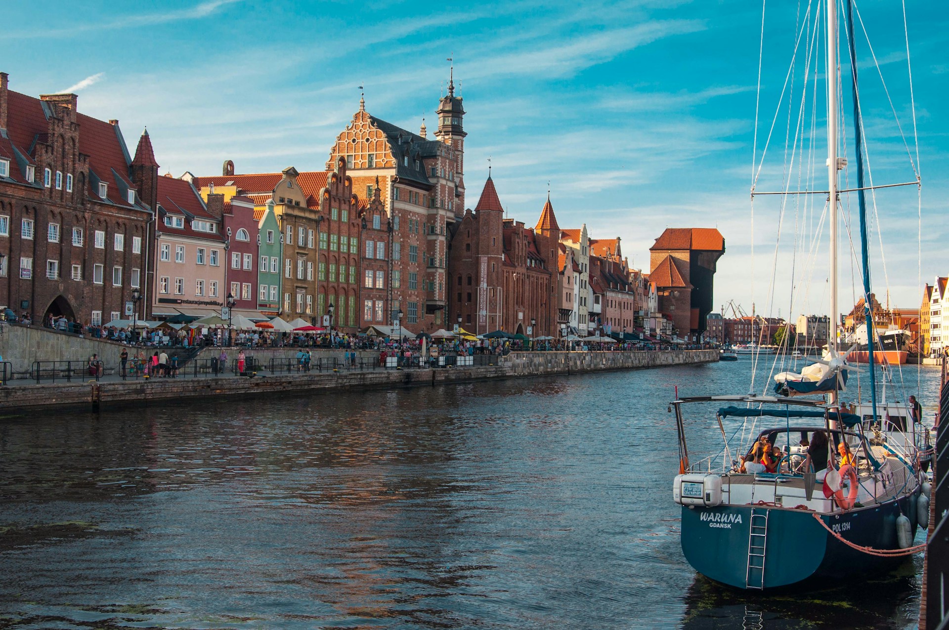 The photo presents the historic waterfront of Gdańsk, Poland, with the Motława River and the medieval Crane in the background.