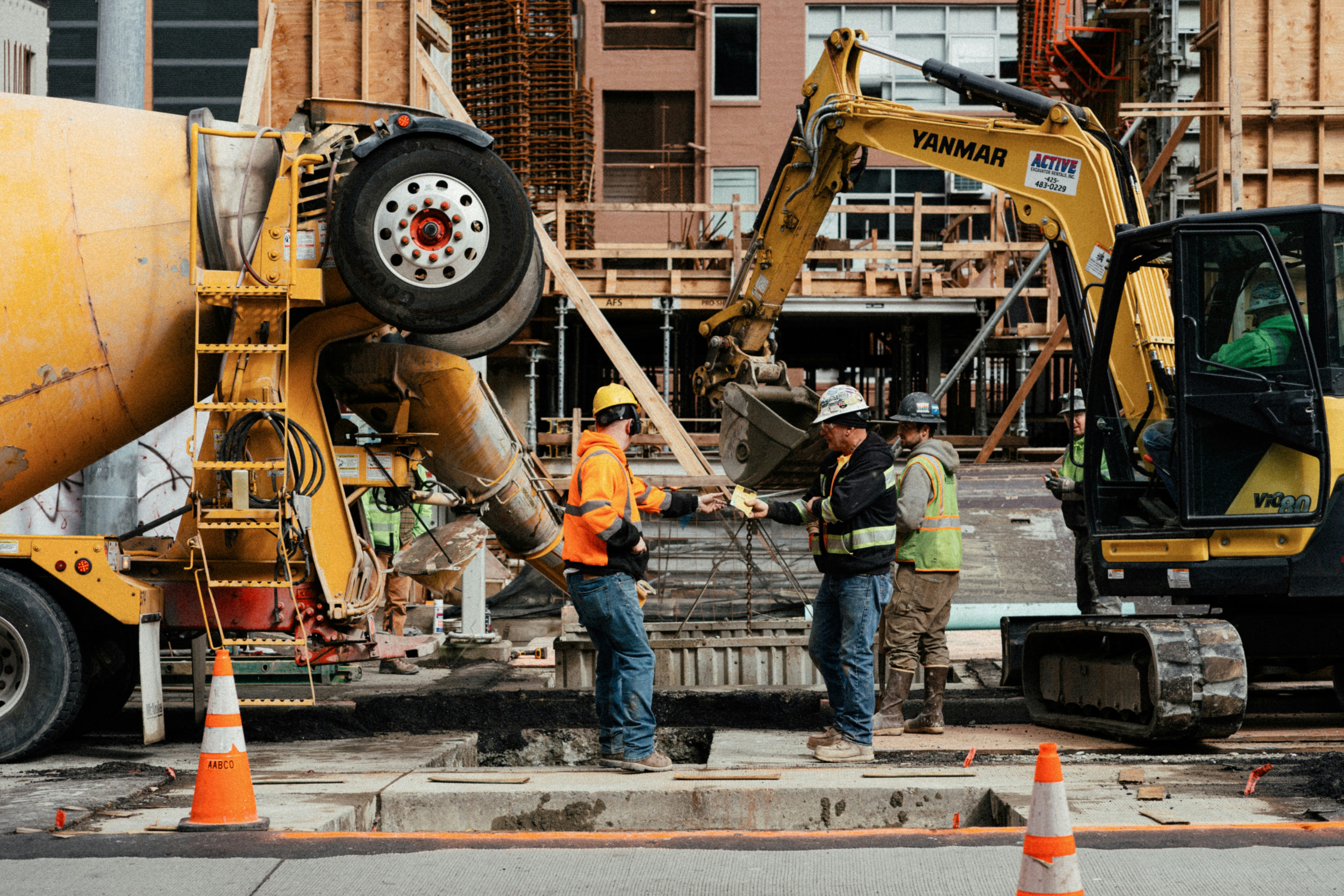 This picture shows an active construction site where workers are coordinating around heavy machinery and concrete works during the structural phase of a building project.