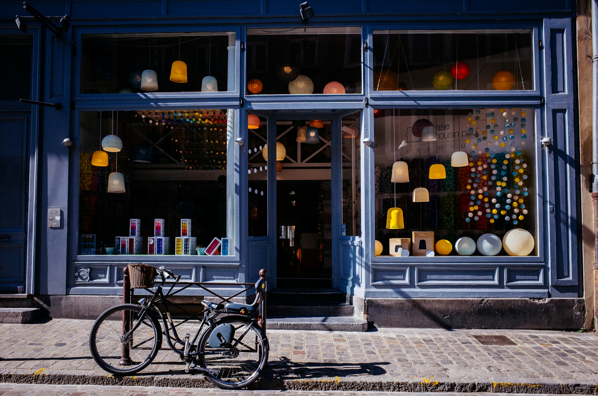 The photo presents the exterior of a small retail shop with decorative lighting and a bicycle parked outside.