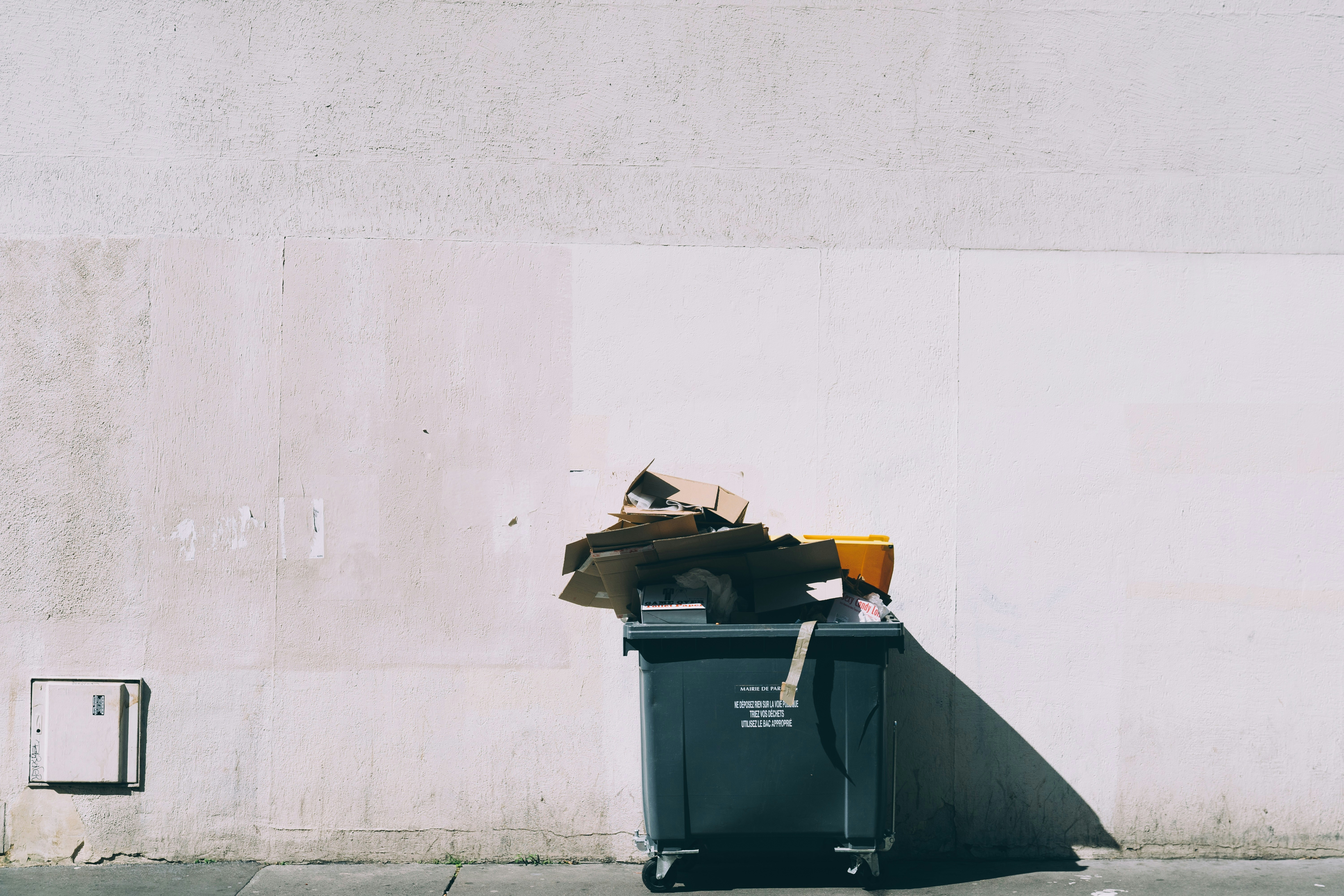 An illustrative photo of black plastic garbage bin with wheels beside wall