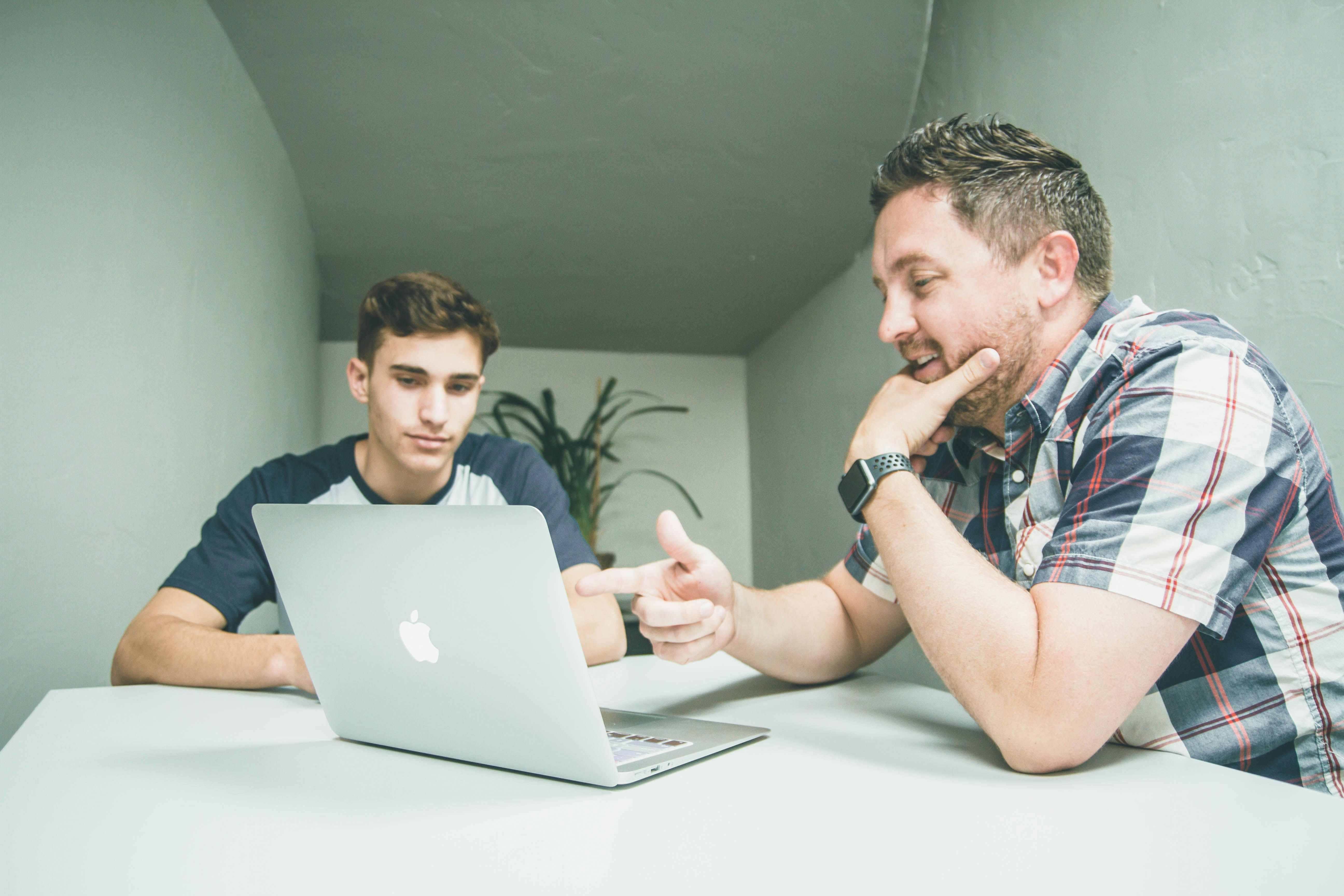 Photo by Unsplash An illustrative photo of a man wearing white and black plaid button up sports shirt pointing the silver macbook