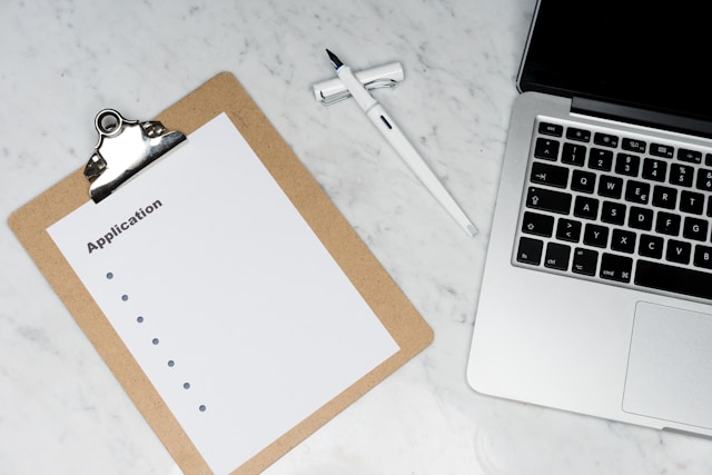 An illustrative photo of a white paper resting on a brown folder beside a silver laptop