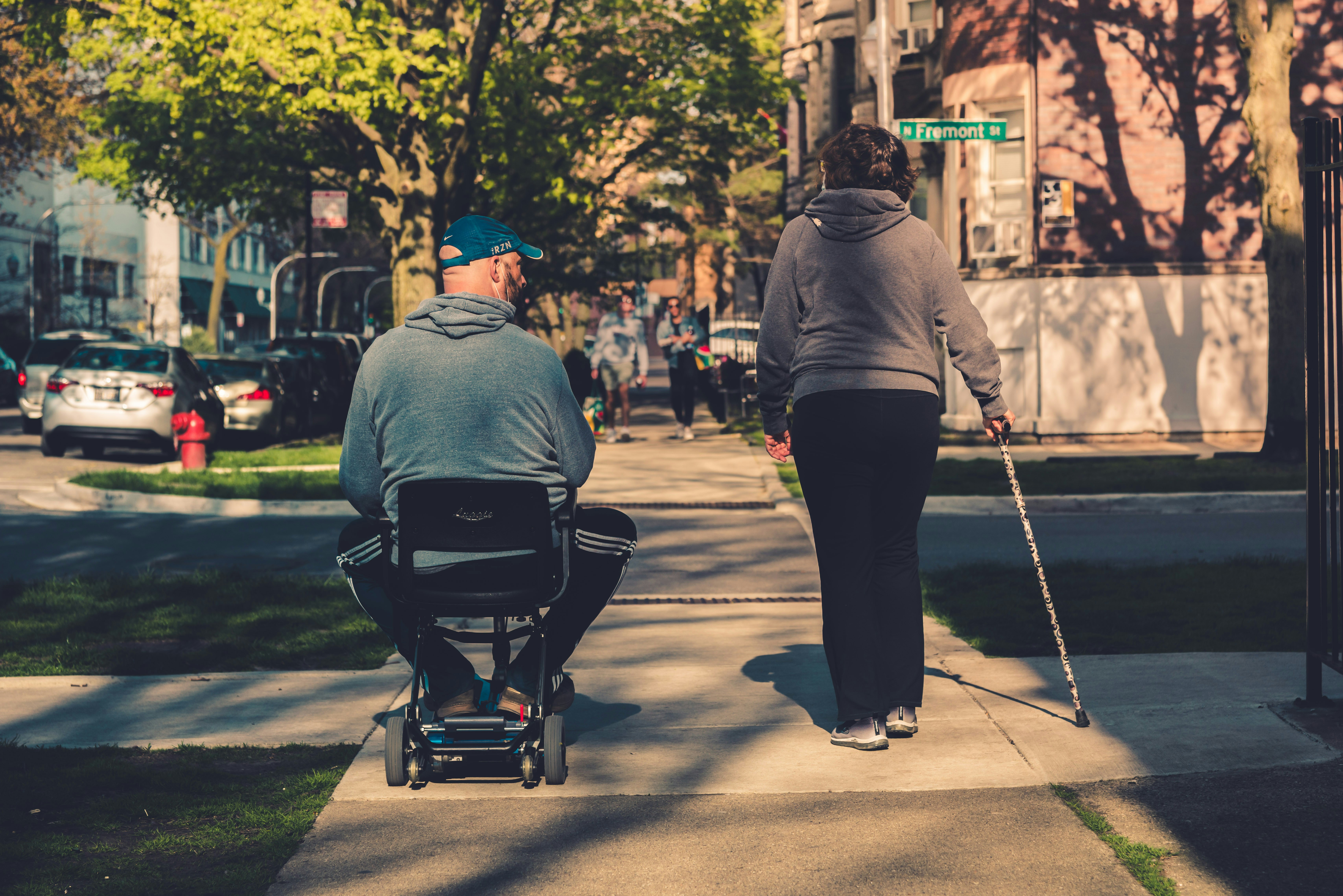 An illustrative photo of a man in a gray hoodie and black pants sitting on a black and gray stroller during the daytime