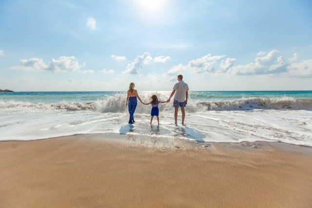 An illustrative photo of a man, woman, and child holding hands while standing on the seashore