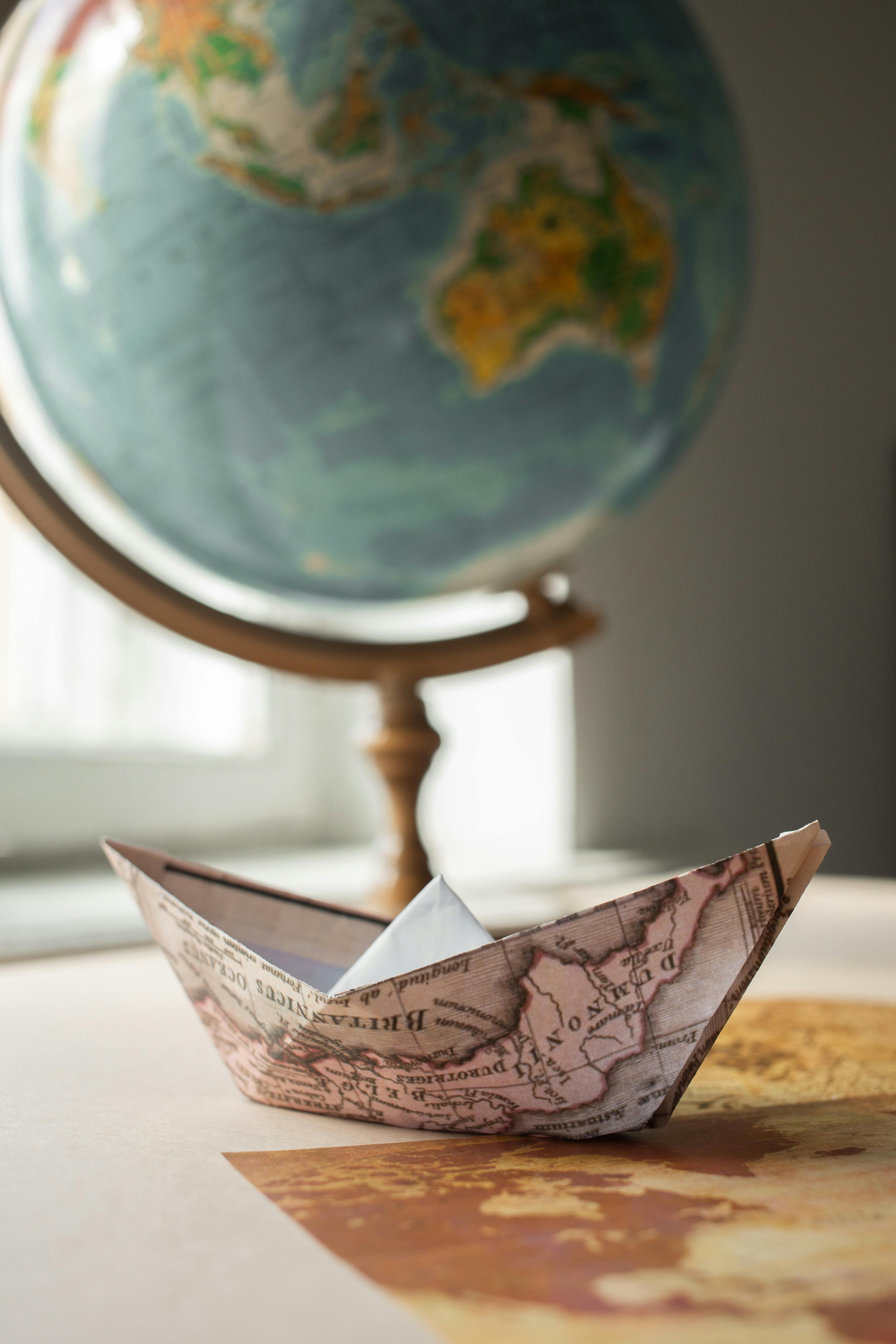 An illustrative photo of a paper boat with map near globe