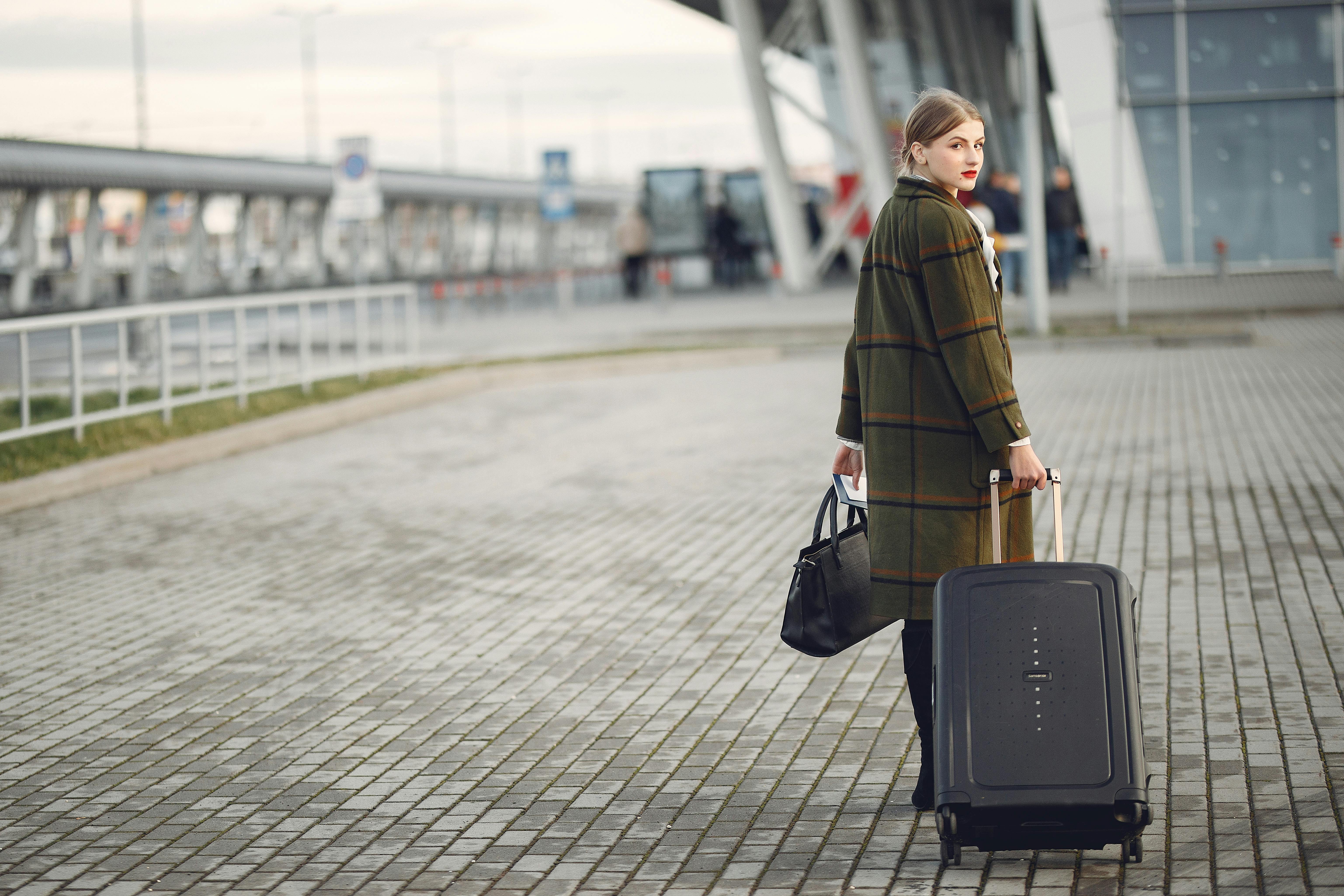 An illustrative photo of the back view of a businesswoman carrying baggage before a flight near an airport building