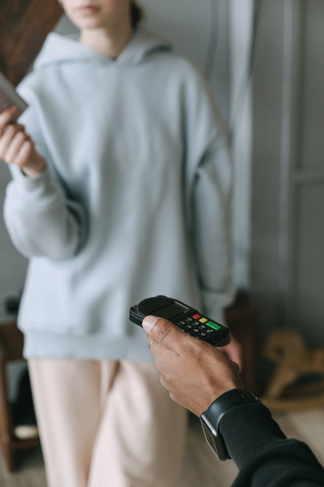 An illustrative photo of a person holding a phone with another person standing and holding a book in the background