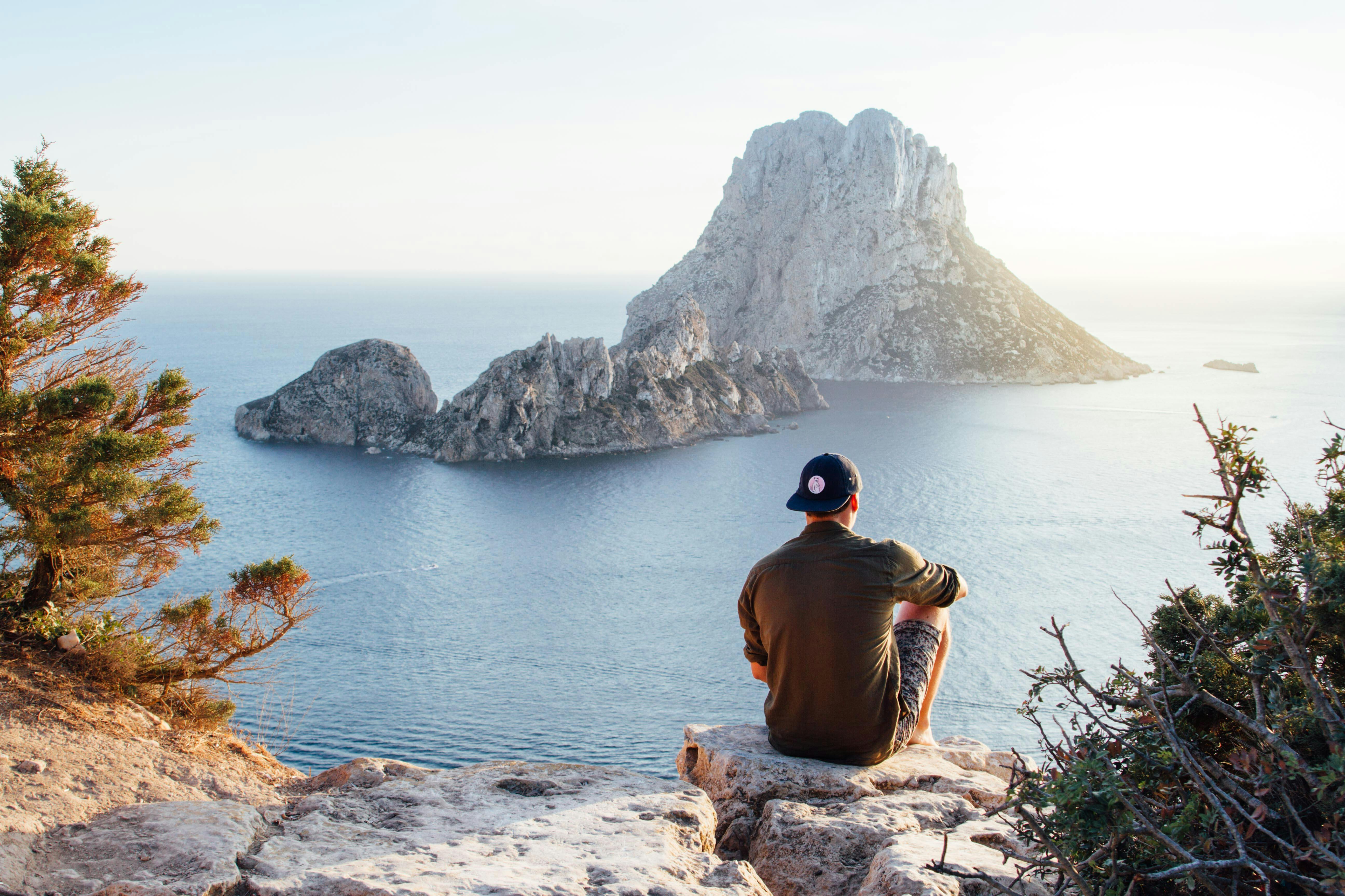 An illustrative photo of the rear view of a man sitting on a rock by the sea.