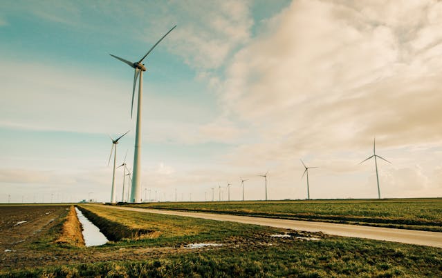 An illustrative photo of windmills standing on a green grass field.