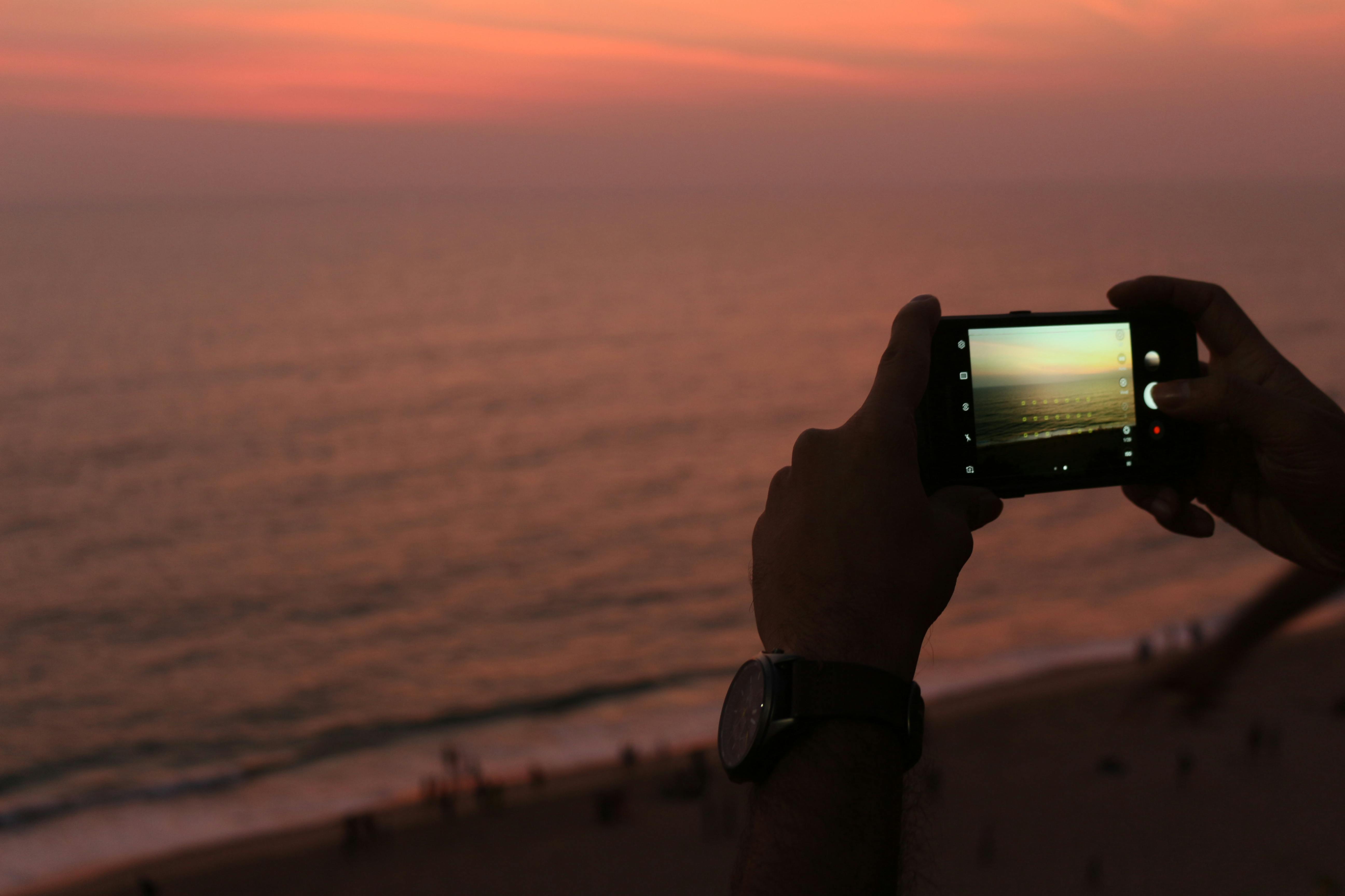 An illustrative photo of a man photographing ocean during sundown