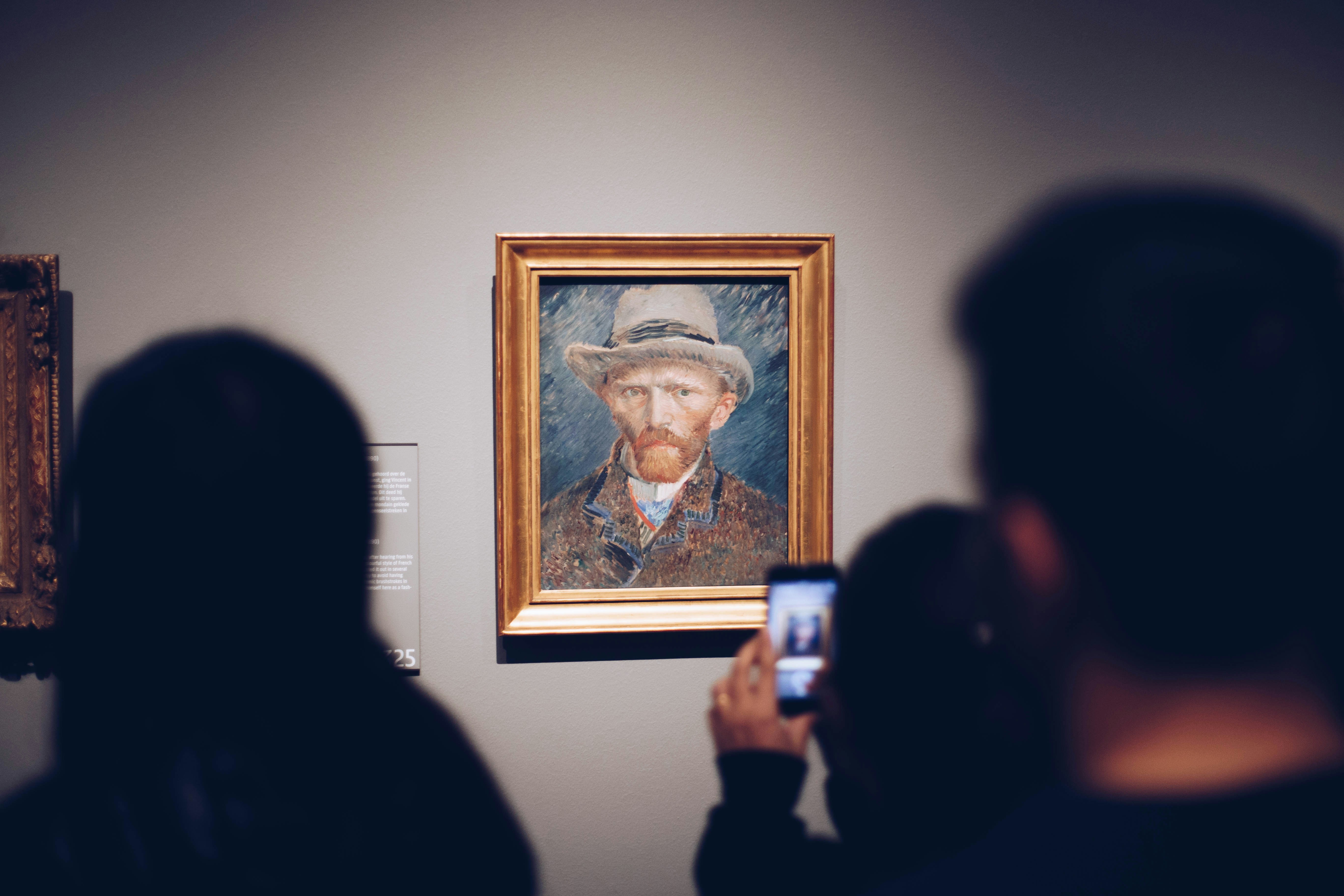 An illustrative photo of a person taking a picture of a man wearing a brown hat and painting