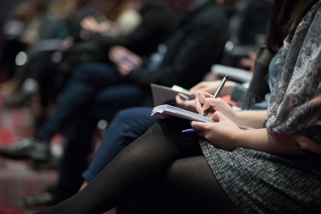 An illustrative photo of people sitting on chairs while writing on notebooks.