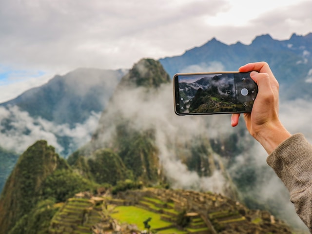 An illustrative photo of a person holding smartphone taking picture of green mountain.