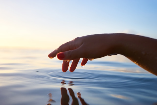 An illustrative photo of a person about to touch the calm water with their hand, creating a serene and reflective moment