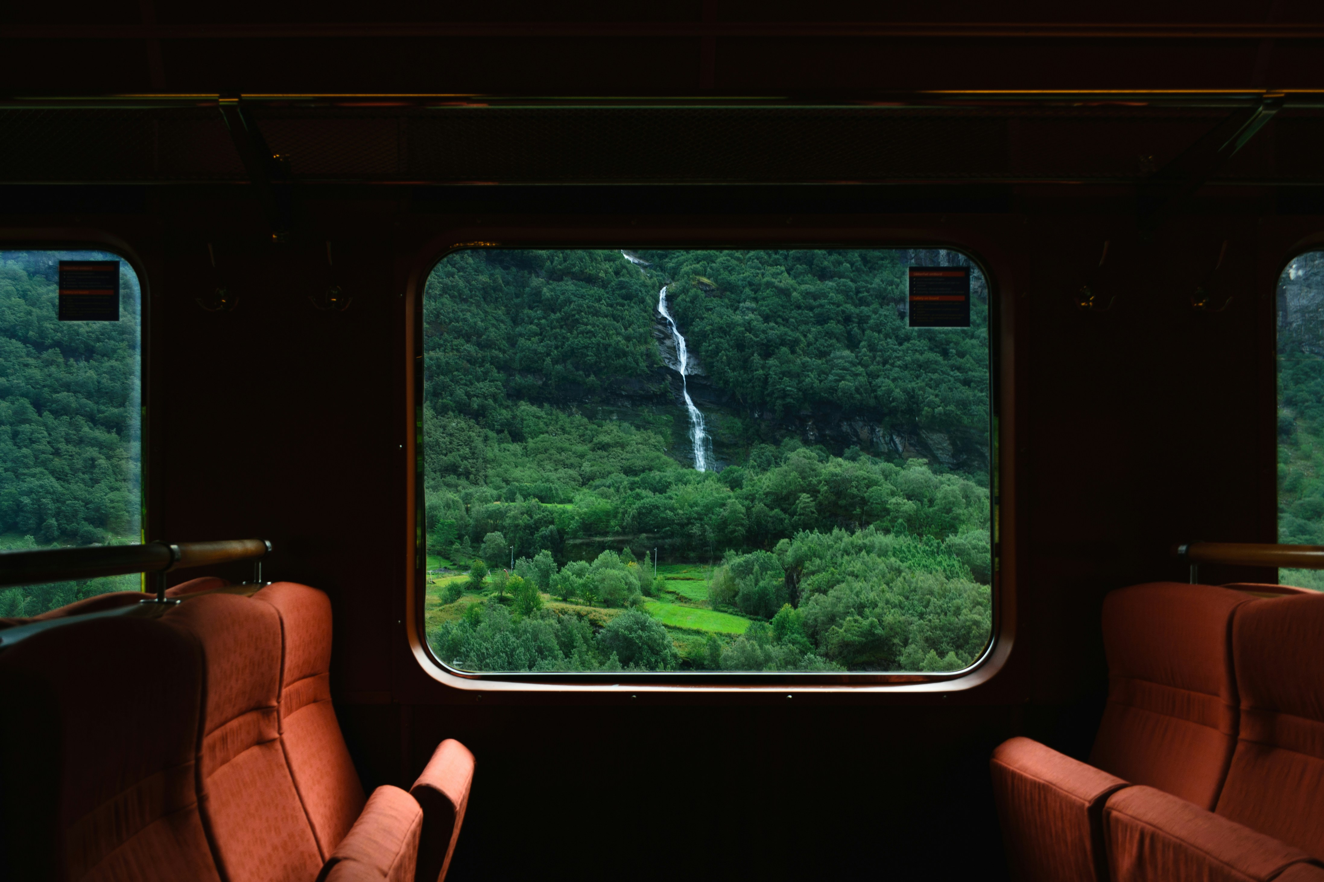 An illustrative photo of a train carriage with two empty red seats facing a large window.