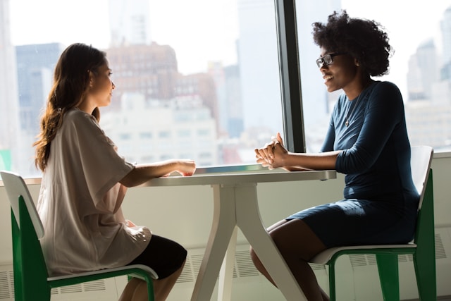 An illustrative photo of two women sitting beside a table, engaged in a lively conversation