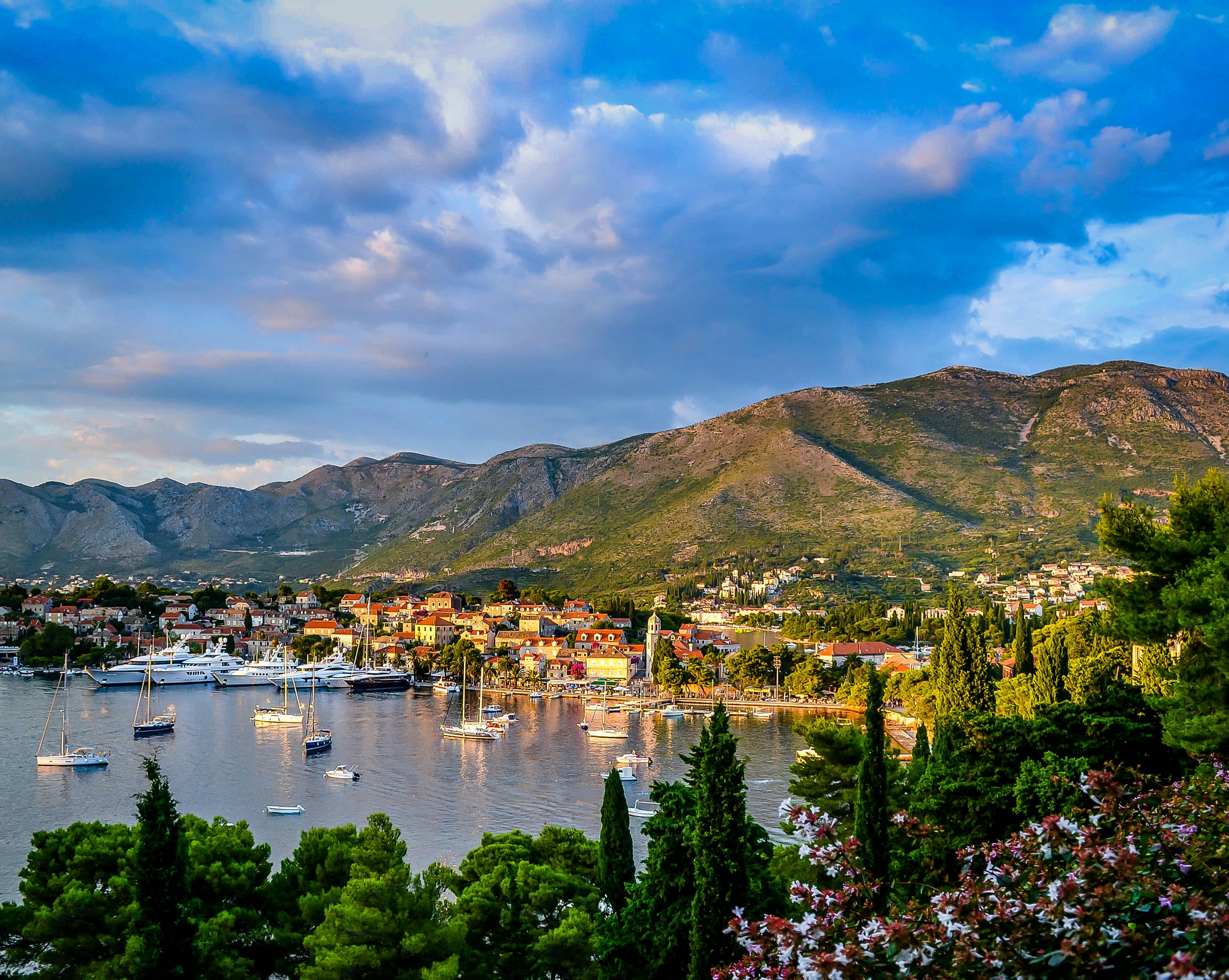 An illustrative photo of boats on body of water surrounded by trees and houses near mountain