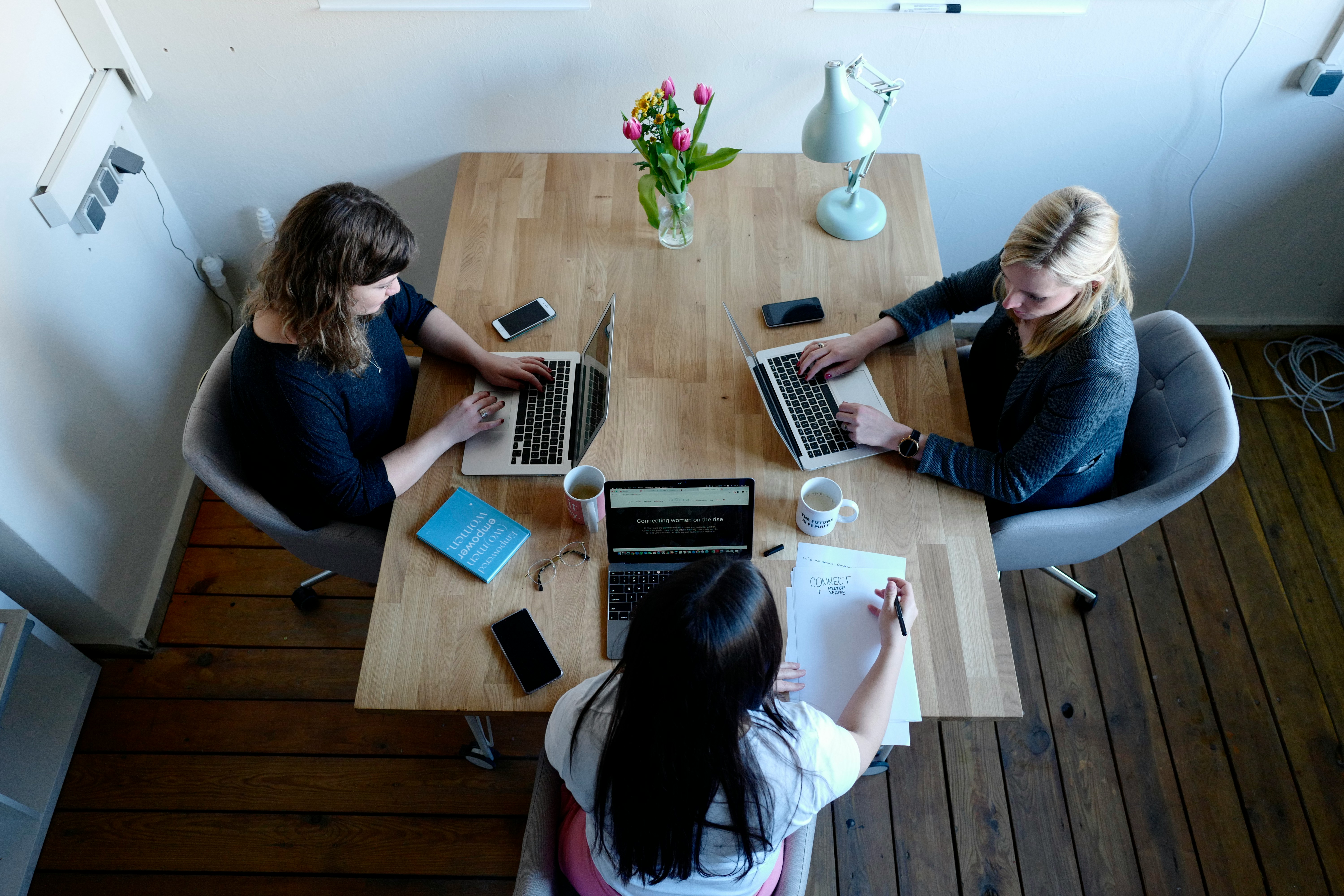 An illustrative photo of three women sitting around table using laptops