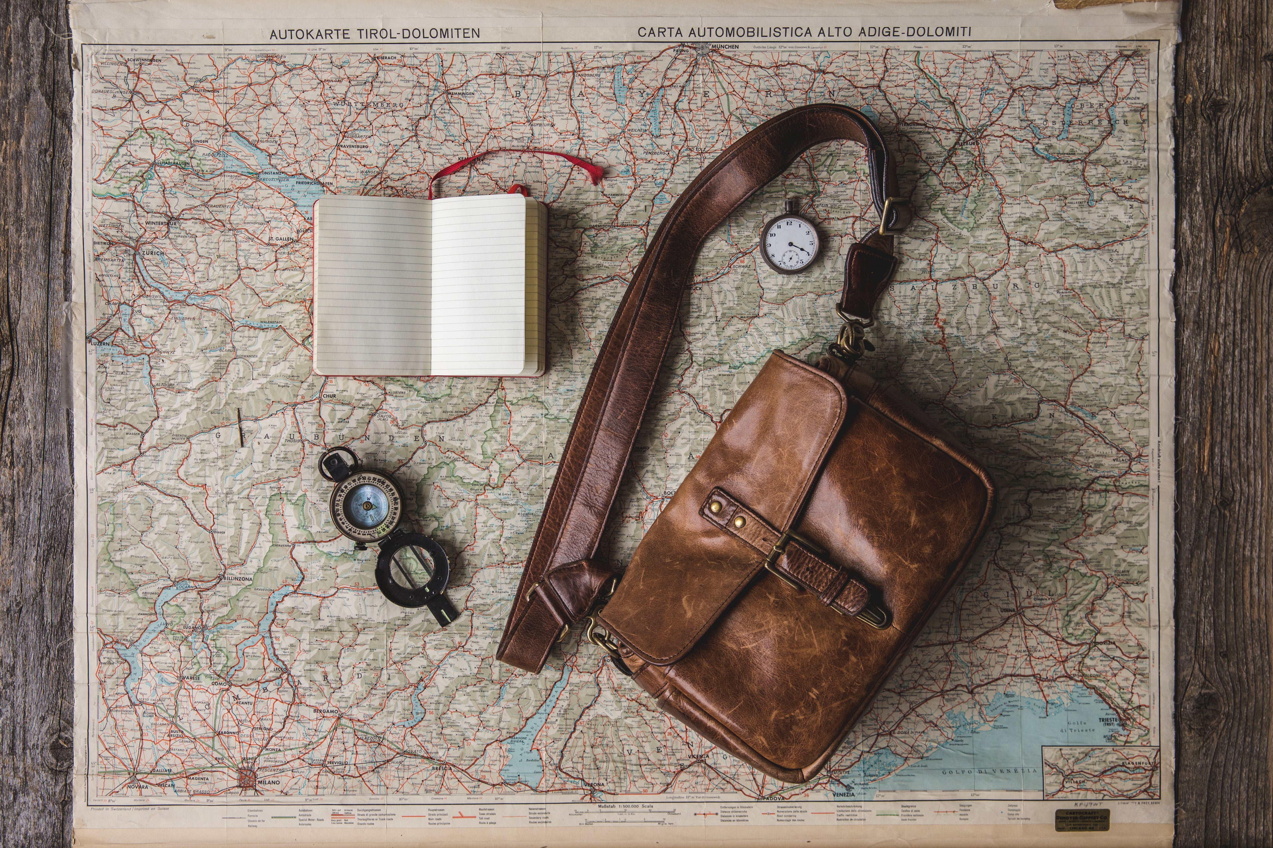 An illustrative photo of a bag, watch and a notebook on a map