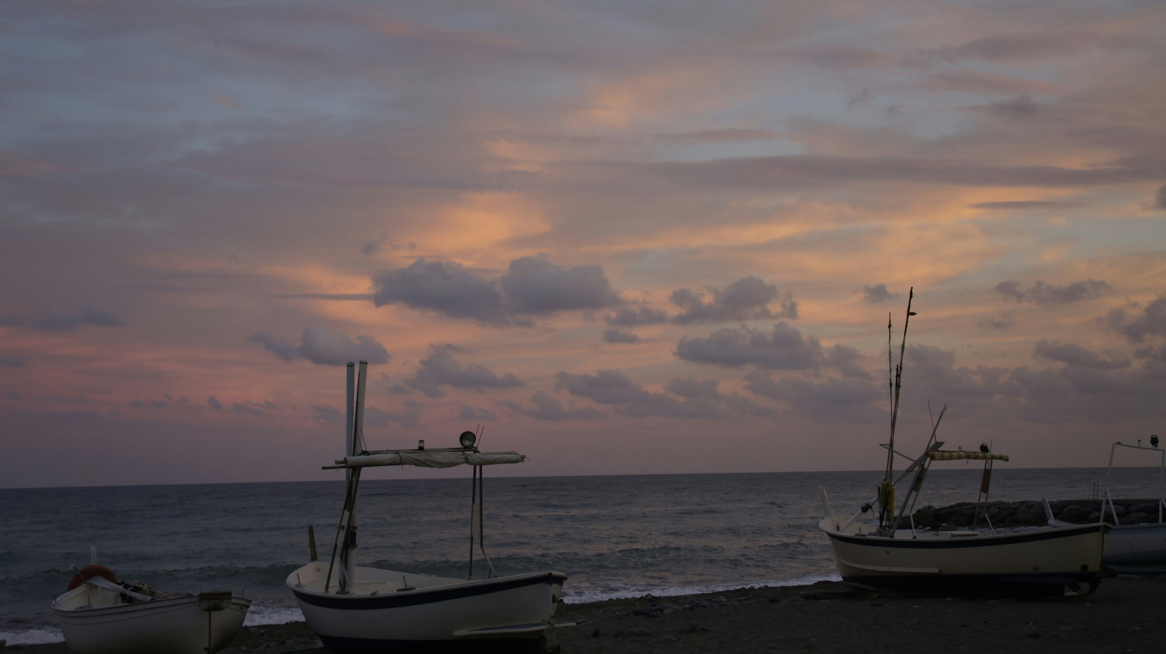 An illustrative photo of a couple of boats sitting on top of a beach during sunset