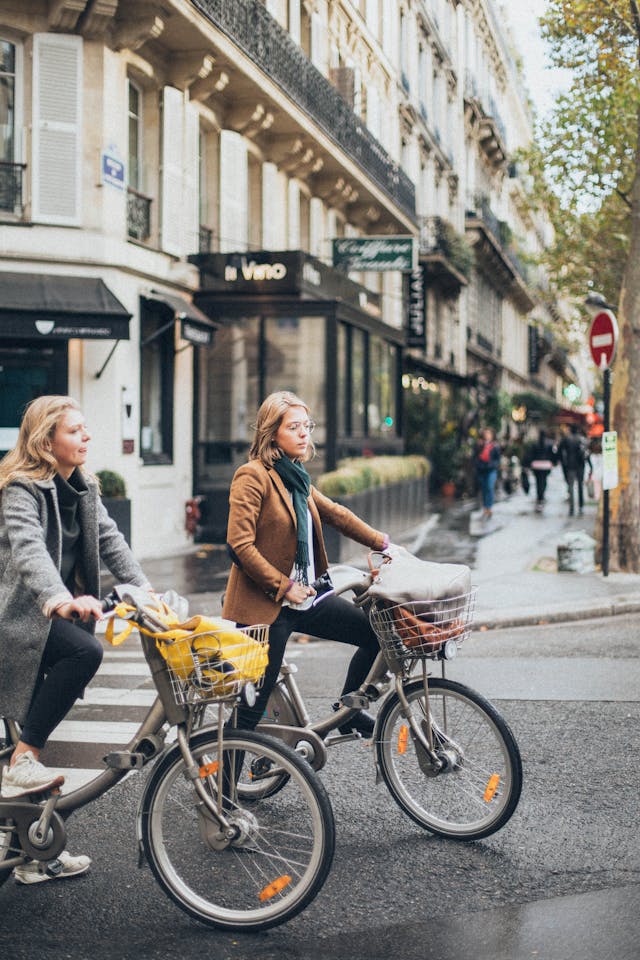 An illustrative photo of two women riding their bikes along a city street