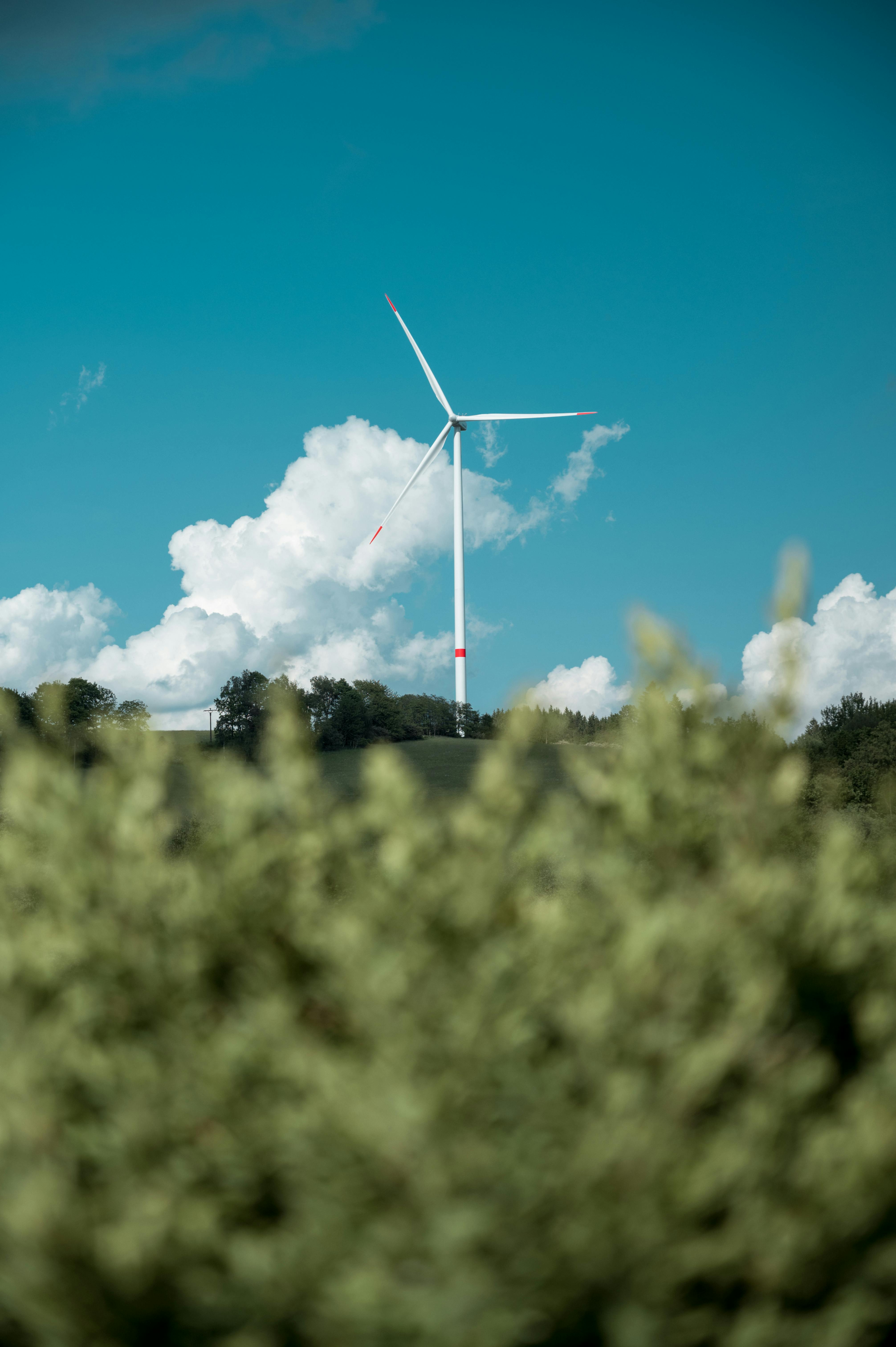 An illustrative photo of a single wind turbine stands tall on a field against a clear blue sky