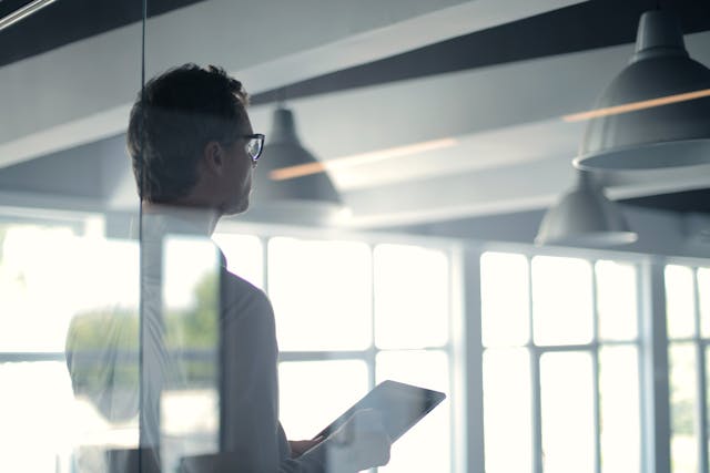 An illustrative photo of a person standing in an office, holding a document or tablet