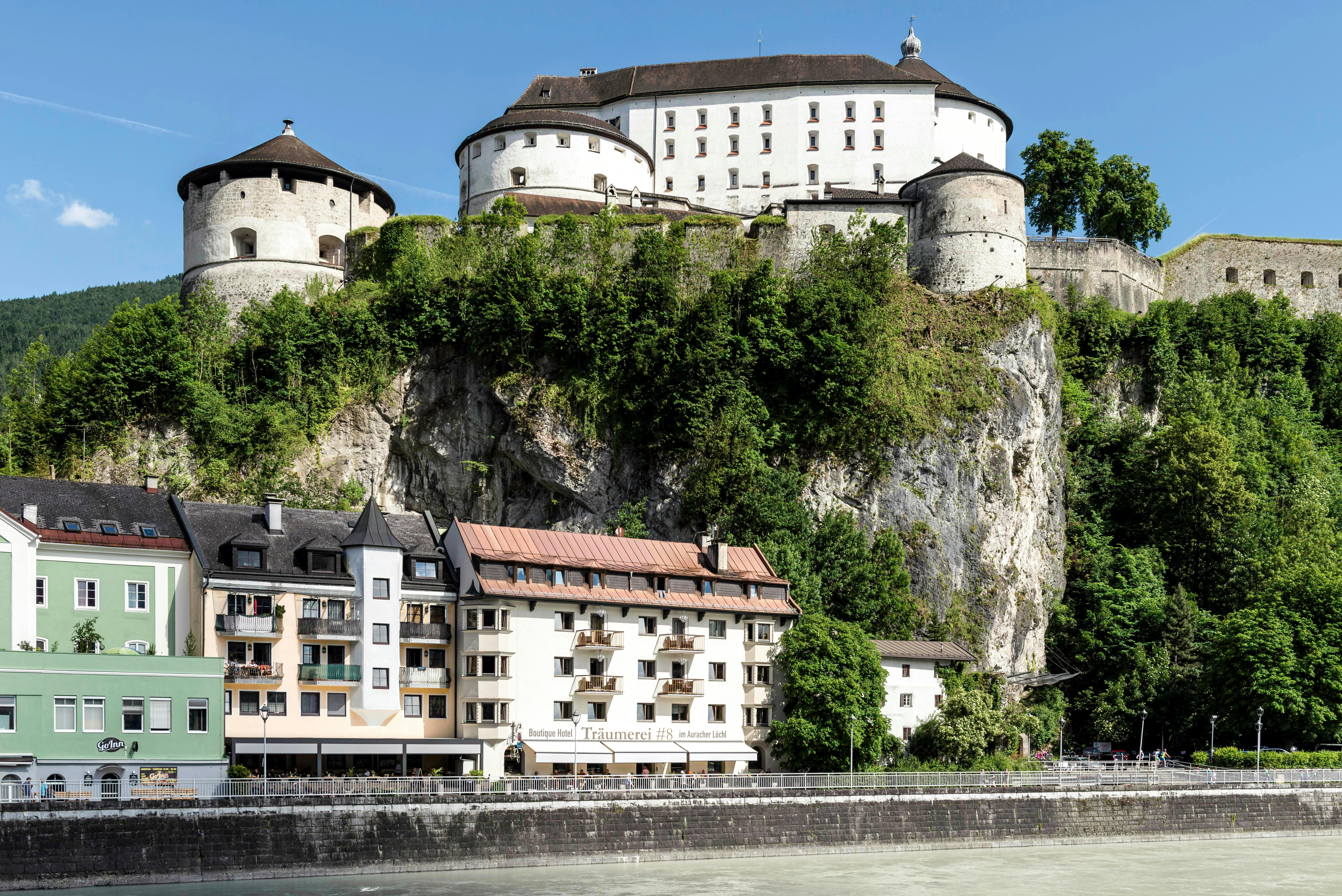 An illustrative photo of large, historic-looking building perched atop a steep rock formation overlooking a body of water