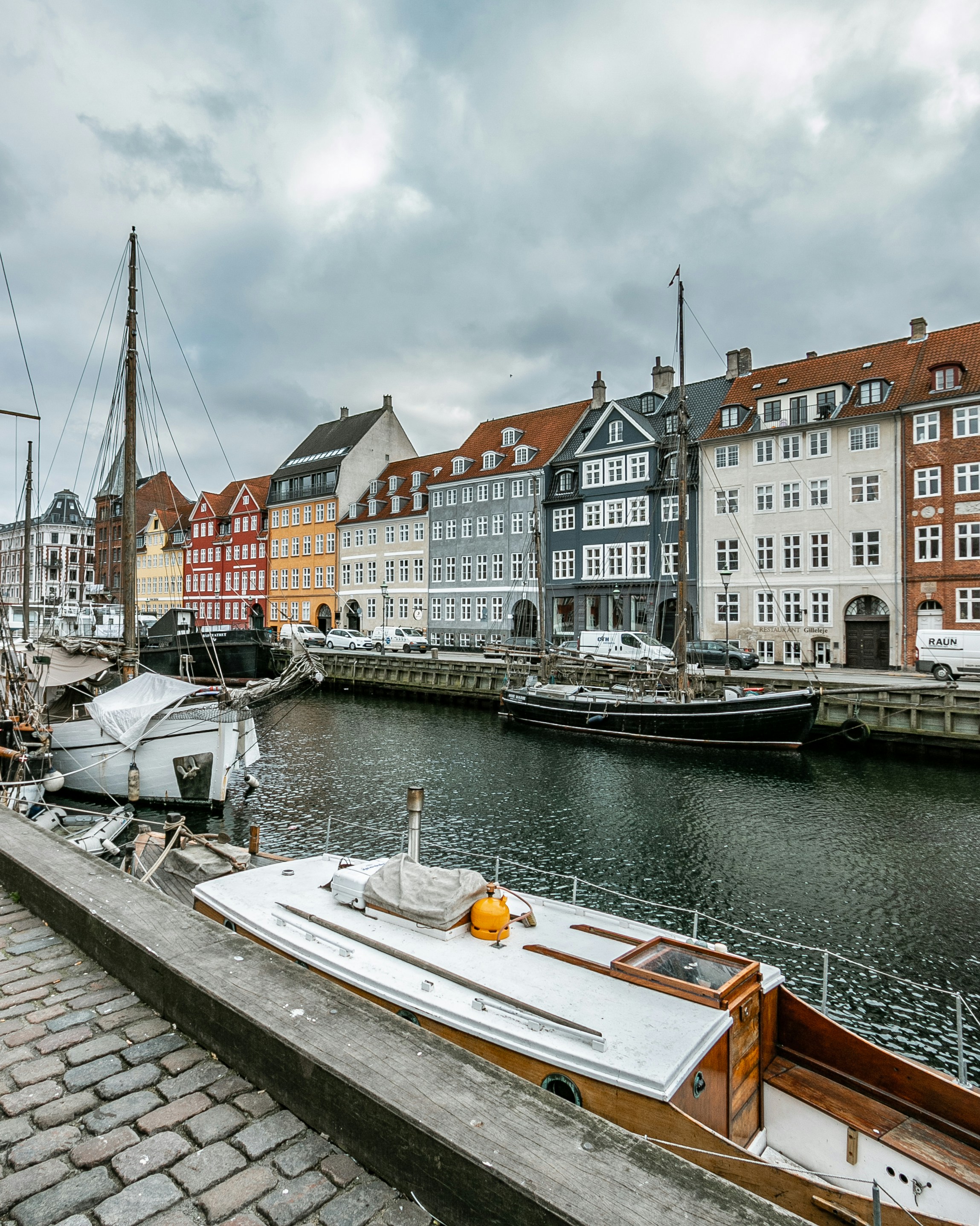 An illustrative photo of a river with boats under cloudy sky near colorful buildings