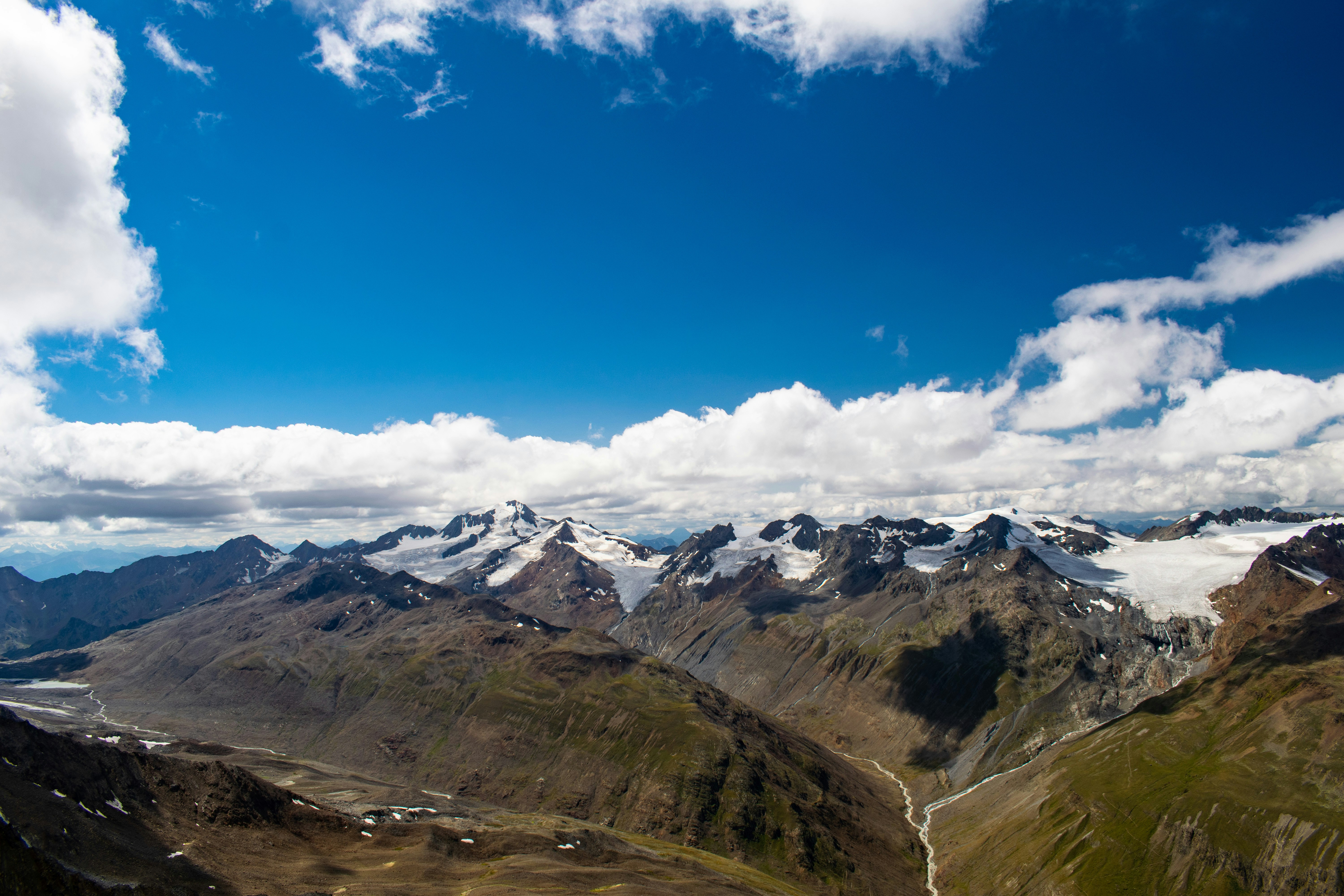 An illustrative photo of mountains with snow on the peaks and a blue sky with white clouds