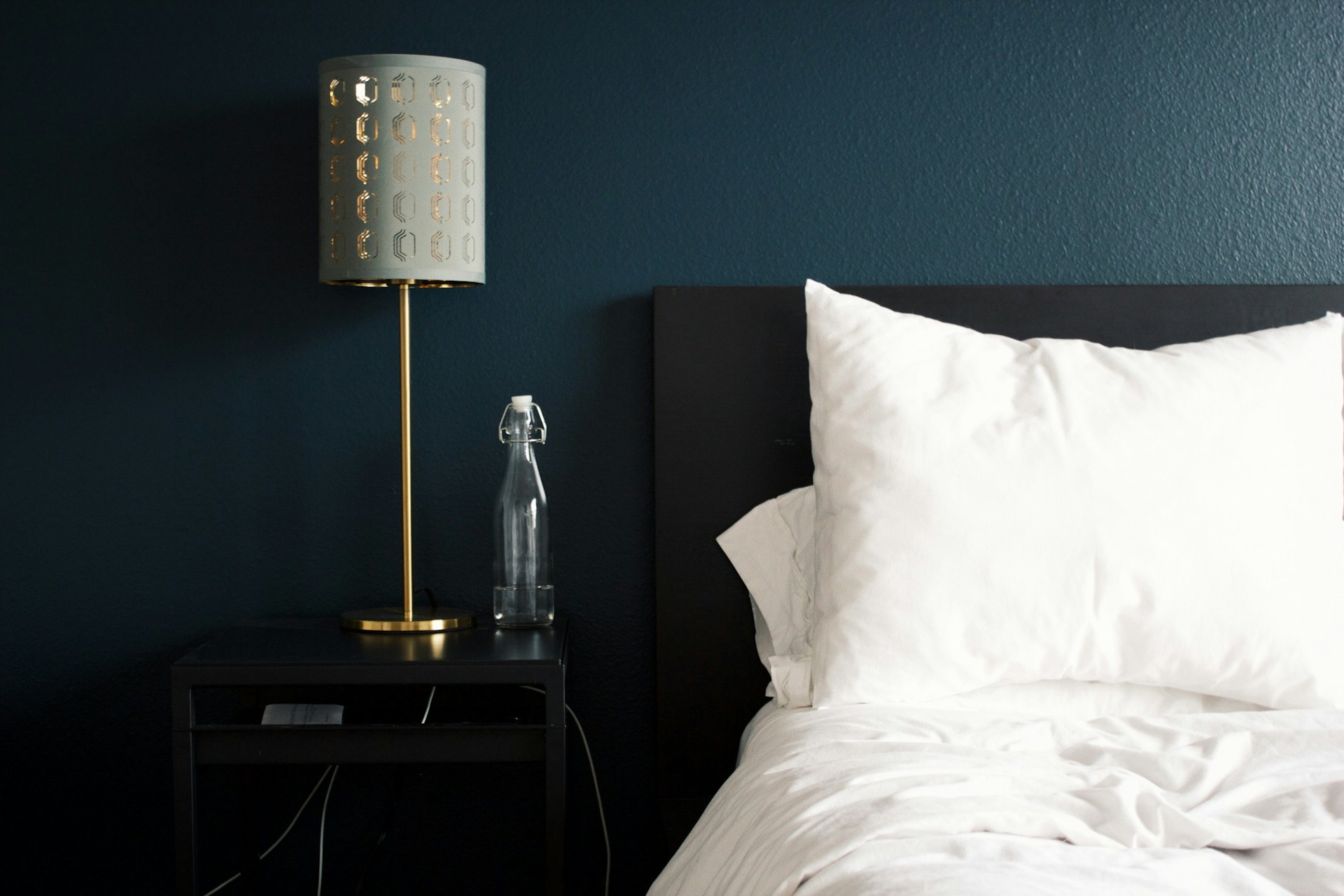 An illustrative photo of a gray table lamp beside white bed pillow