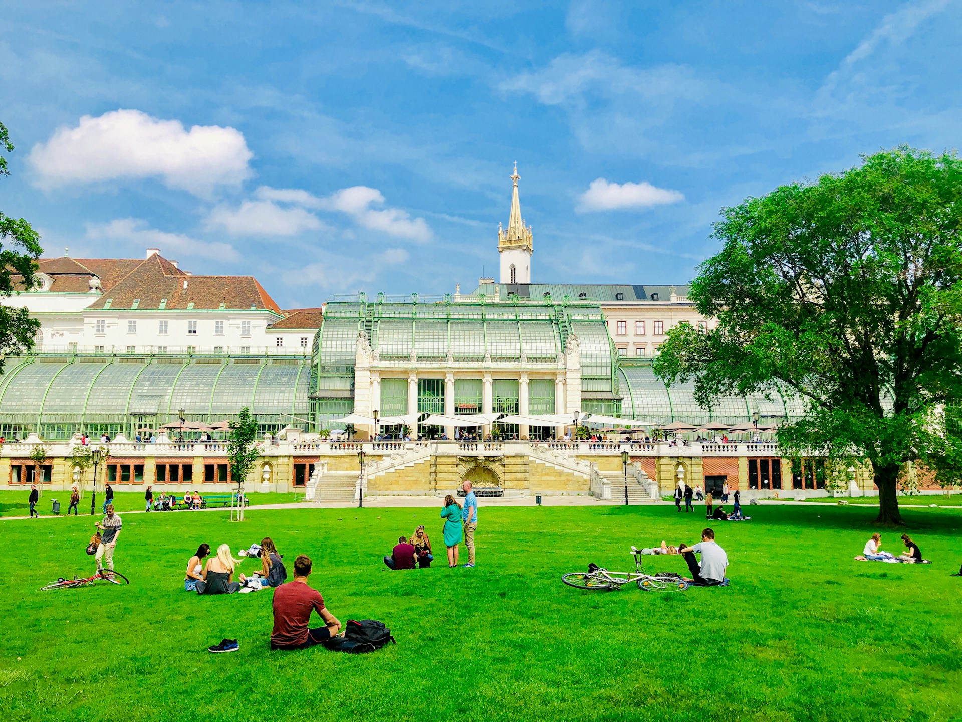 An illustrative photo of people sitting on green grass field near white building in Vienna