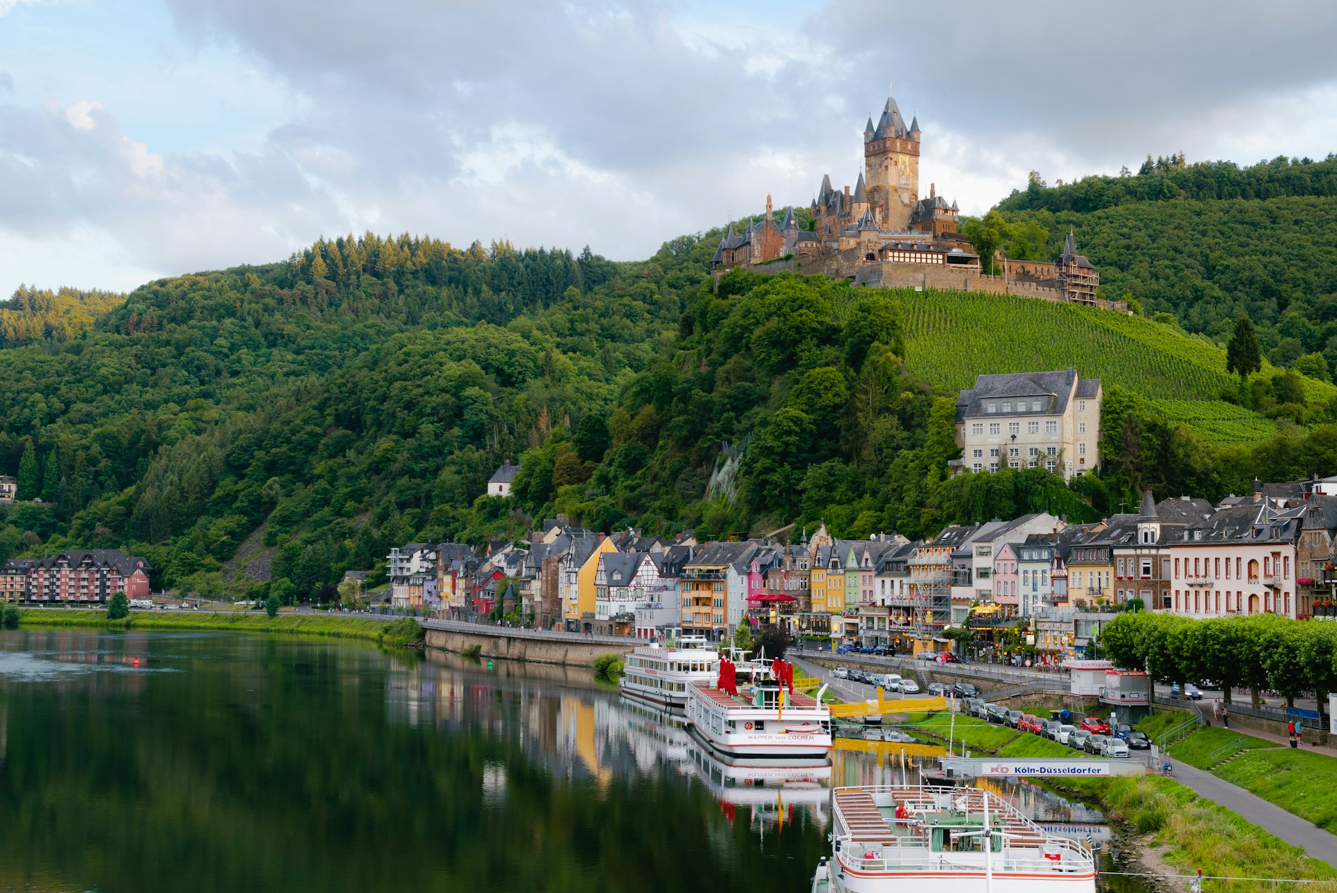 An illustrative photo of buildings near a body of water and a green hill