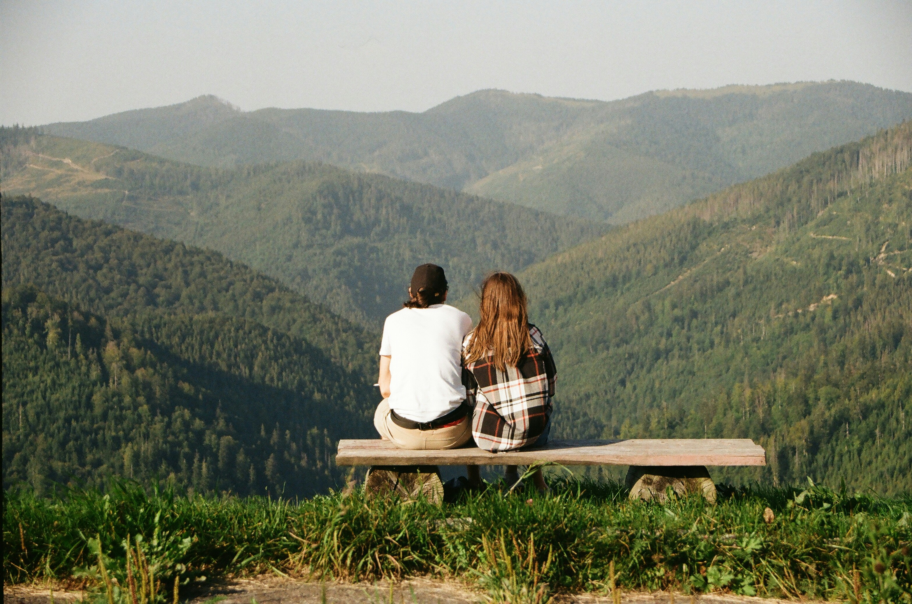 An illustrative photo of a man and a woman sitting on a bench looking at the mountains