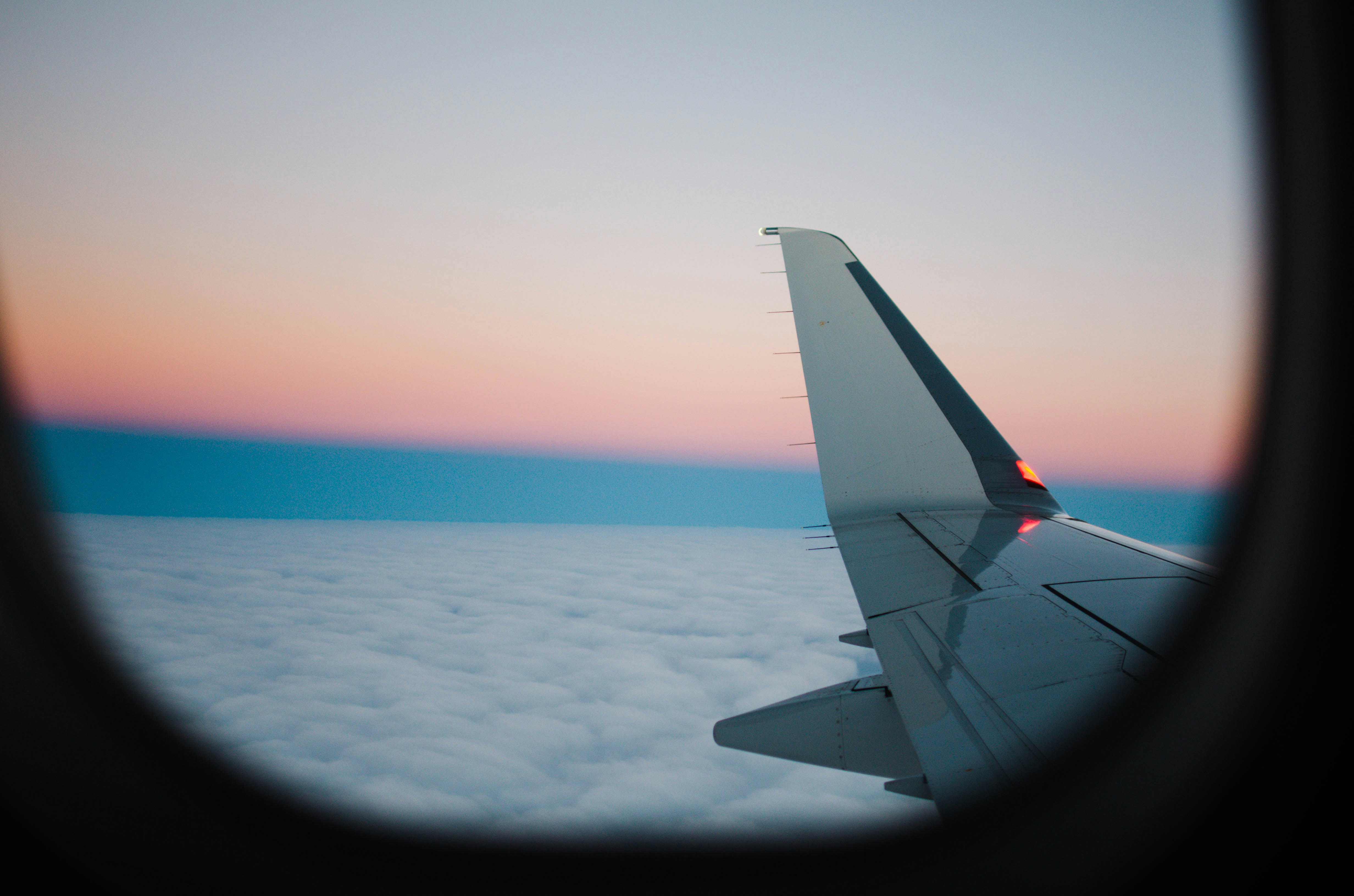 An illustrative photo of a white airplane wing above white clouds.