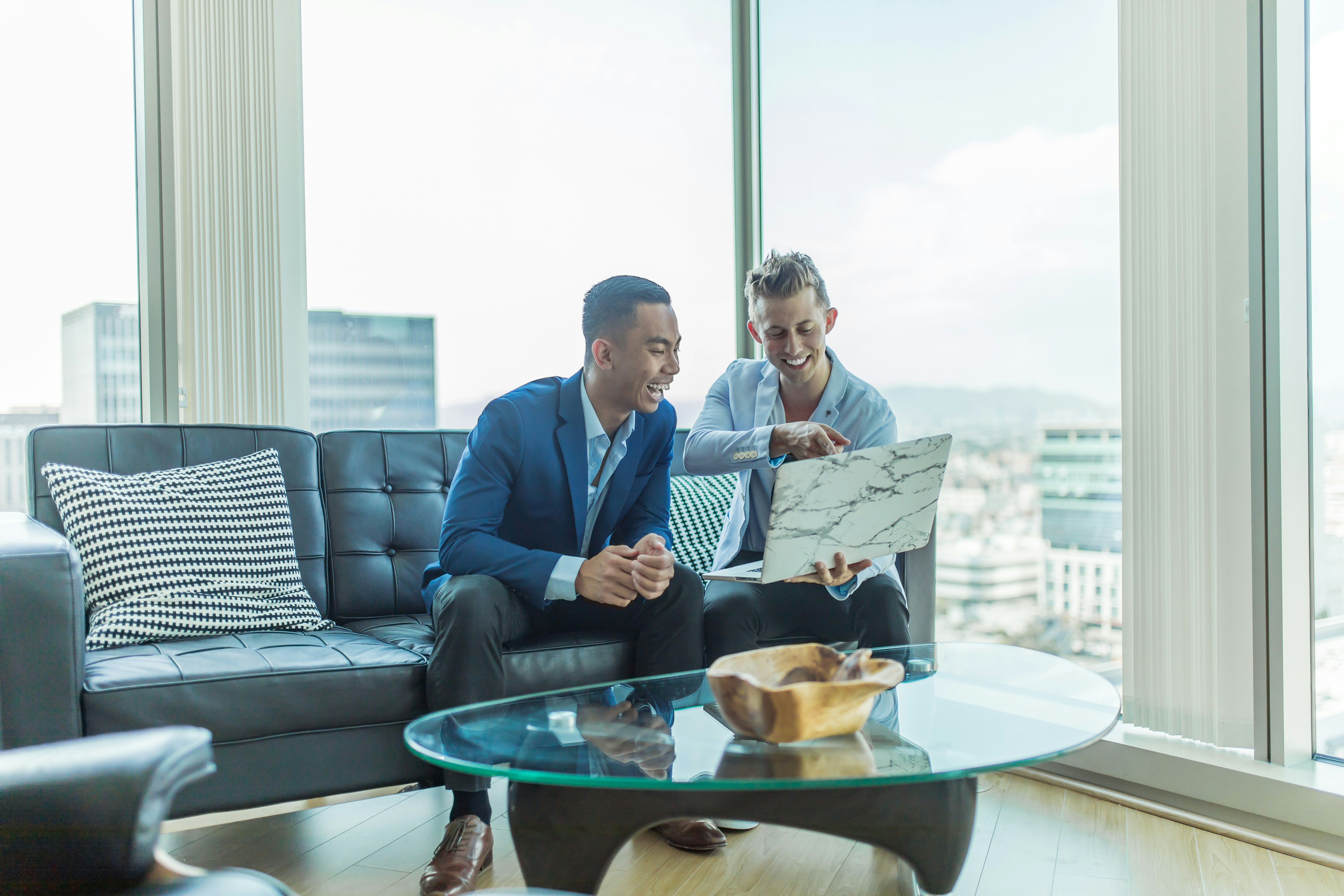 An illustrative photo of two men sitting on a sofa looking in the laptop.