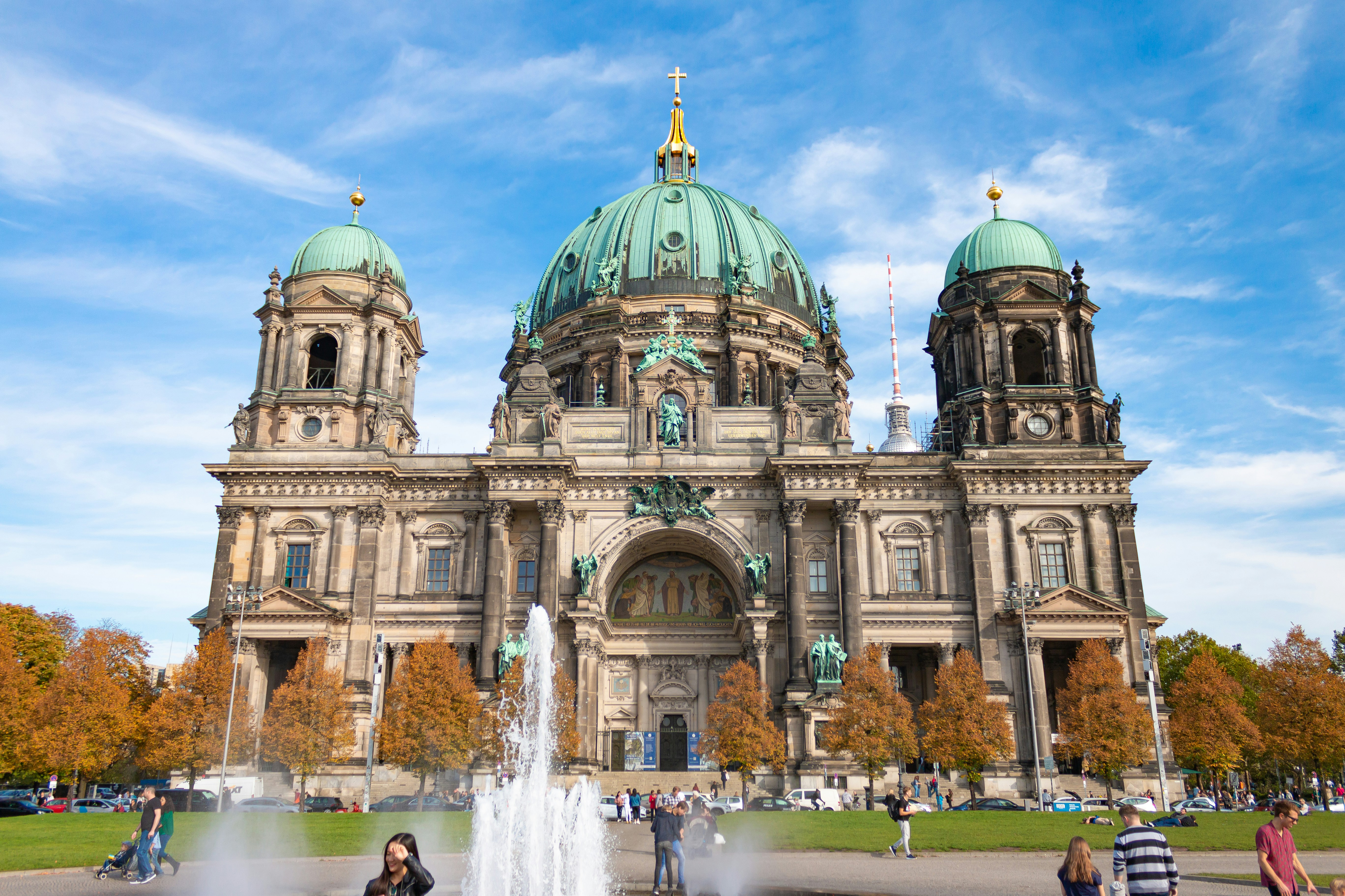 An illustrative photo of people walking near a fountain in front of a grey building.