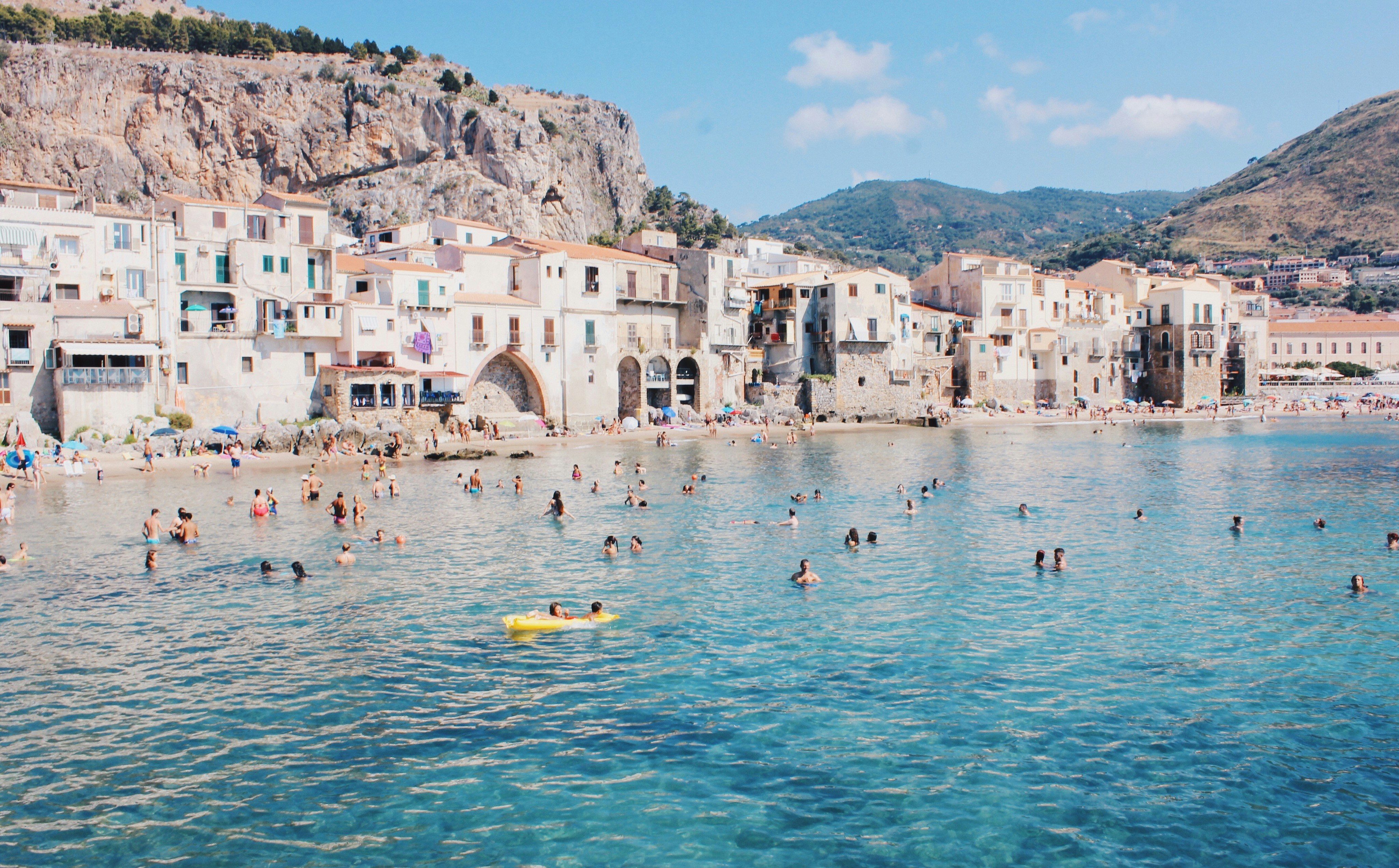 An illustrative photo of people swimming in a sea near a beach with buildings