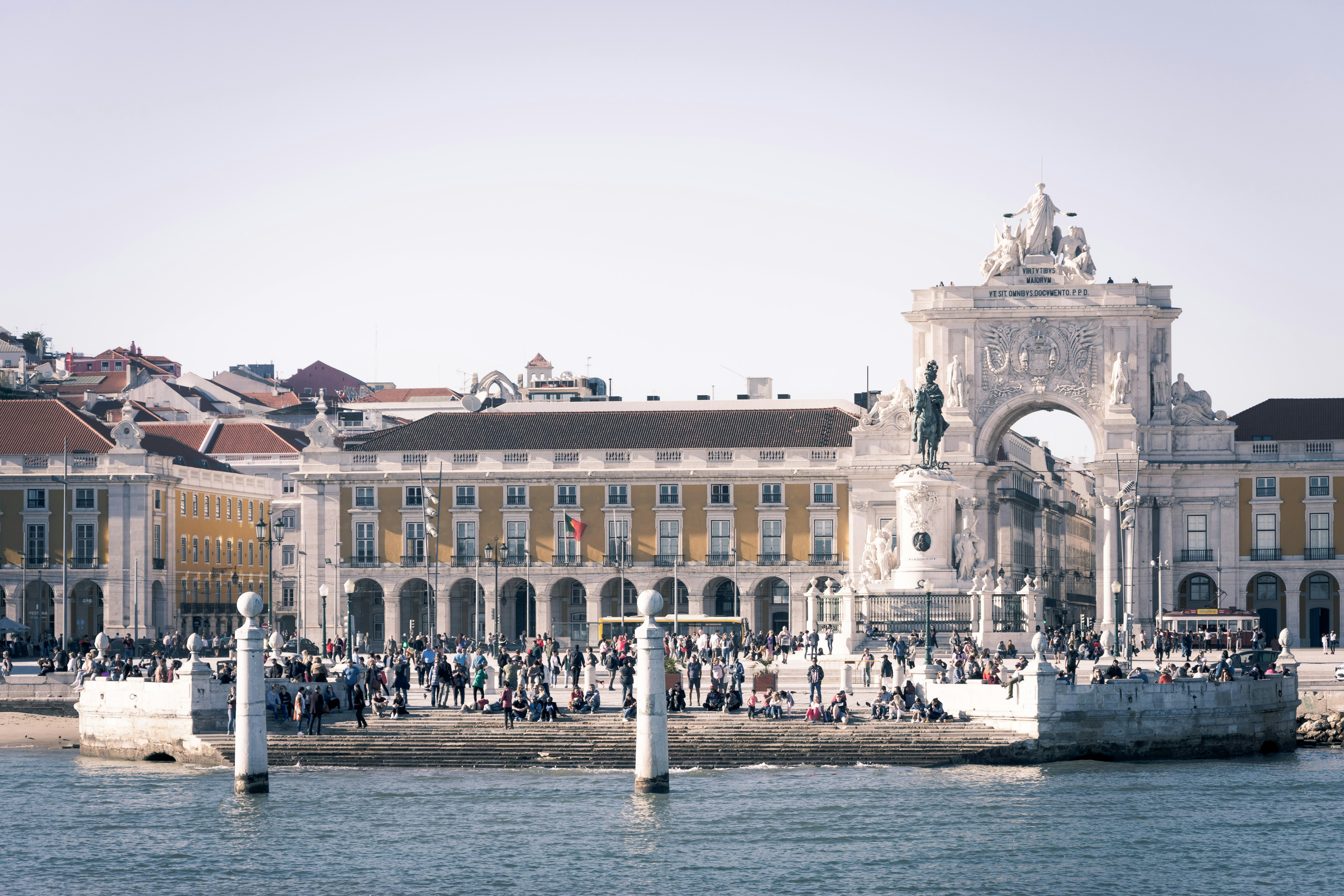 An illustrative photo of people walking near white concrete building near a body of water.