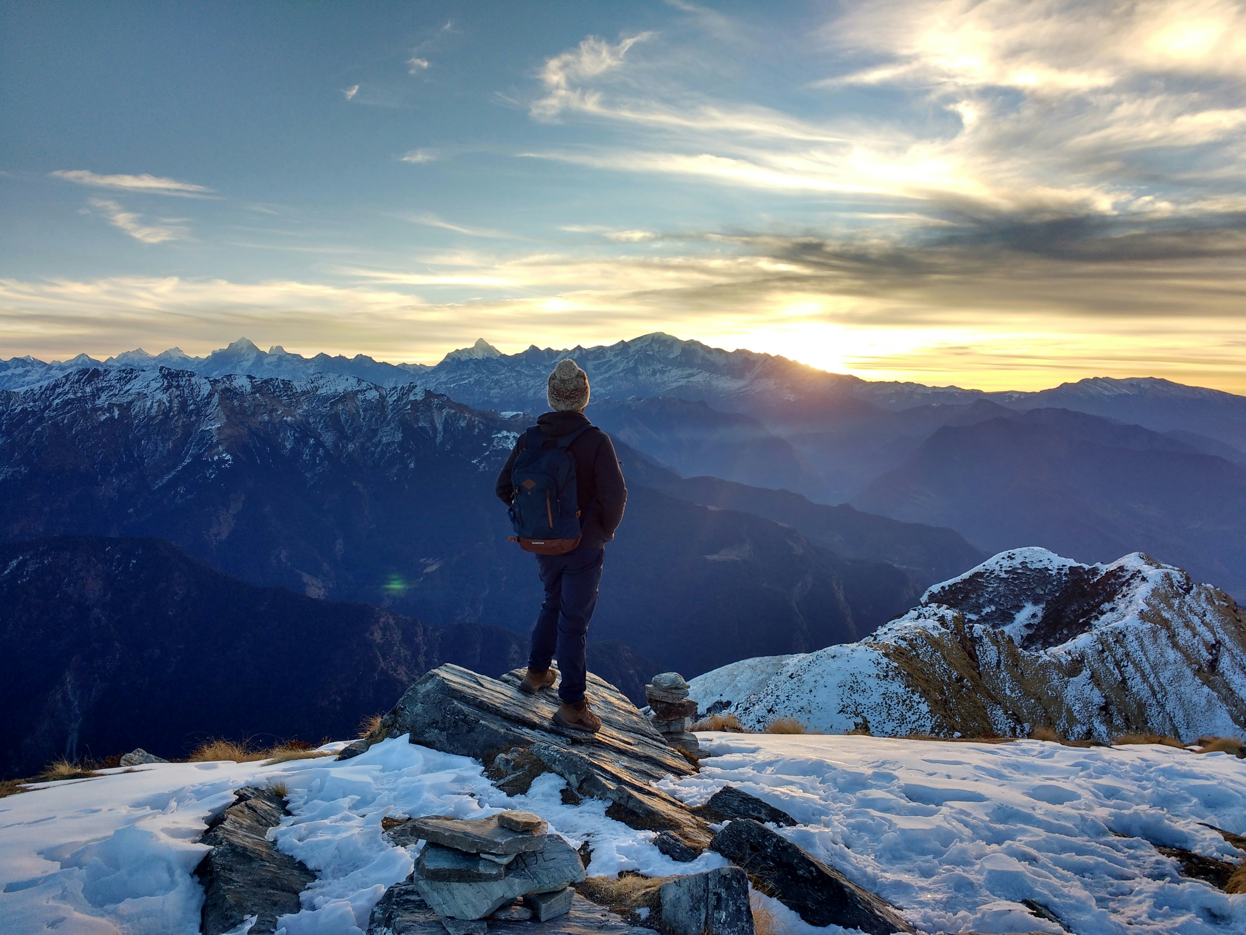 An illustrative photo of person standing on top of the mountain facing sunrise.