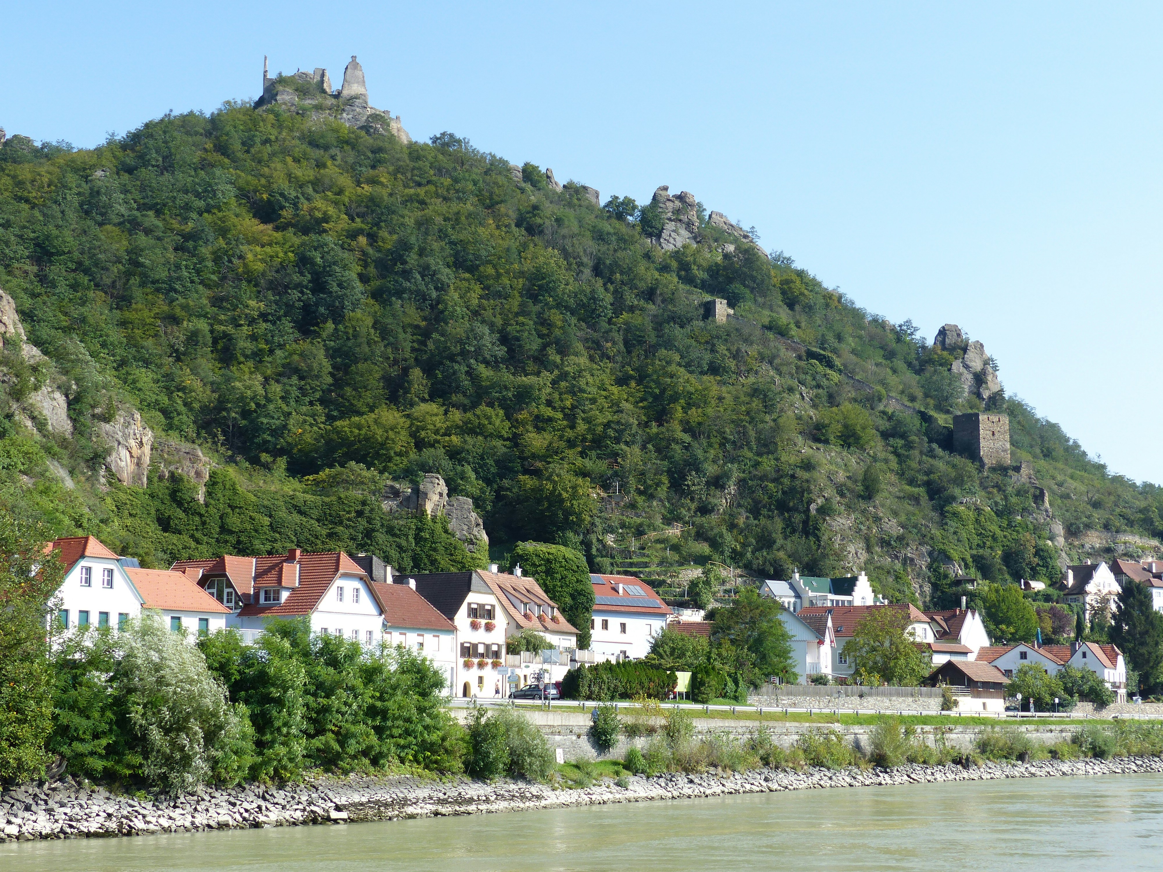 An illustrative photo of white houses on a green hill near a body of water.
